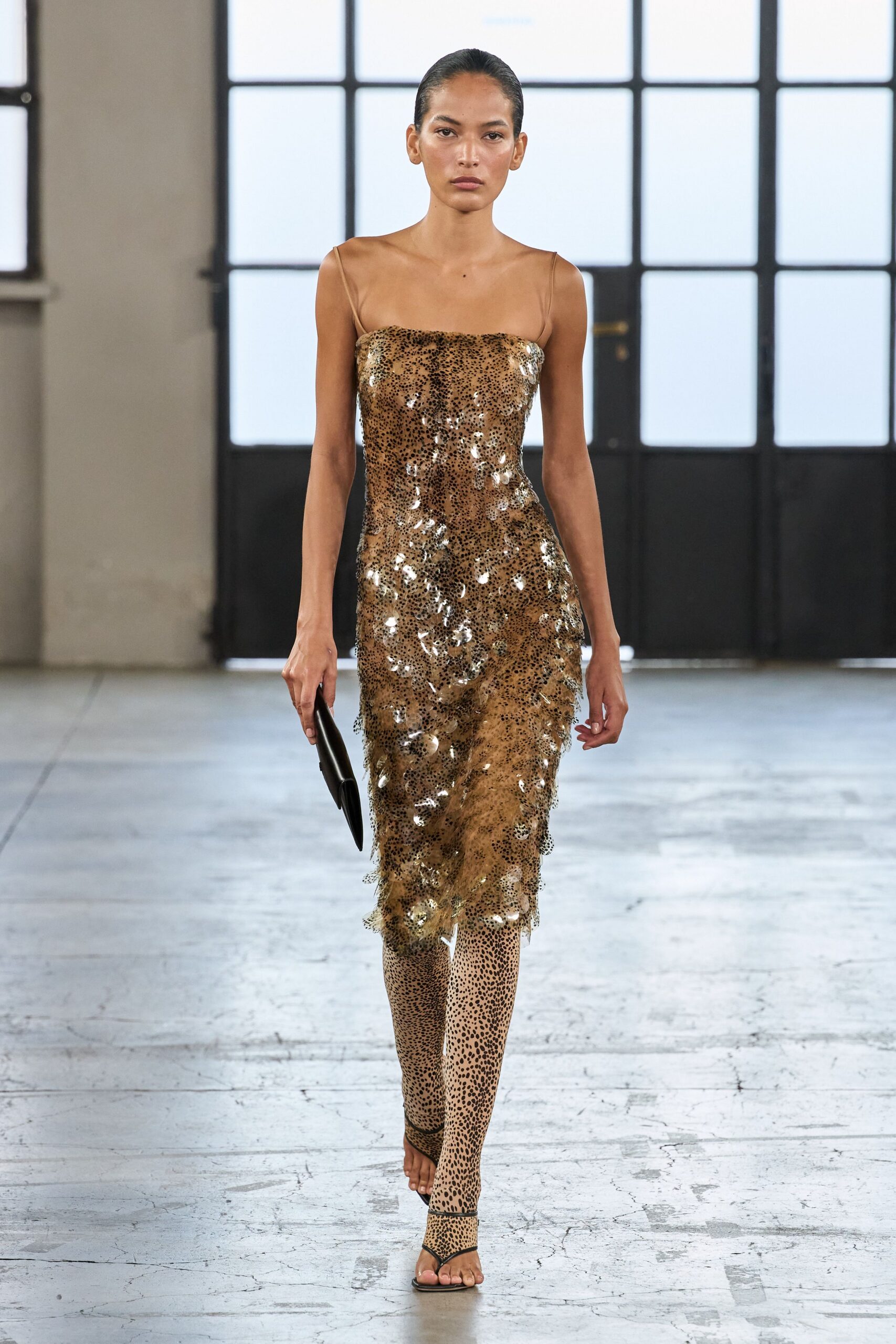 Tan mesh slip dress crusted with silver paillettes over tiny leopard spots. Matching spotted tights, denser at the shin. Black thong sandals with a bare, nearly invisible sole. Flat black clutch tucked under one hand. Crossing a hotel lobby at noon, still dressed from last night's dinner.