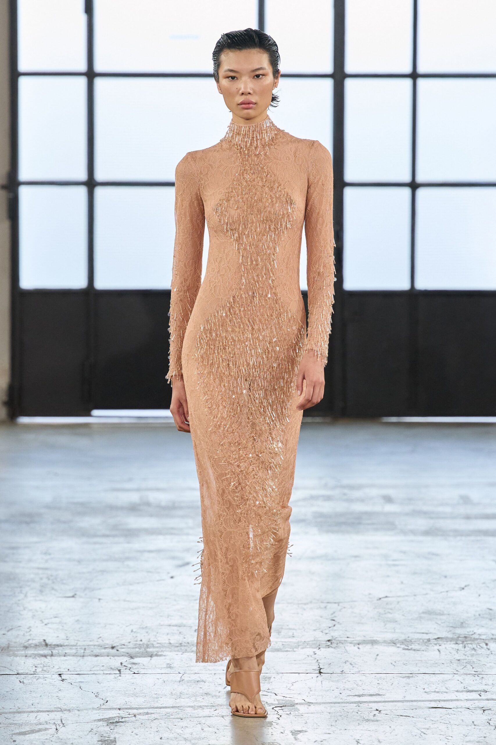Blush lace column gown with bead-fringe spilling from throat to hem. Nude leather toe-loop sandals with a broad folded vamp. Crossing a museum atrium after the string quartet has packed up.