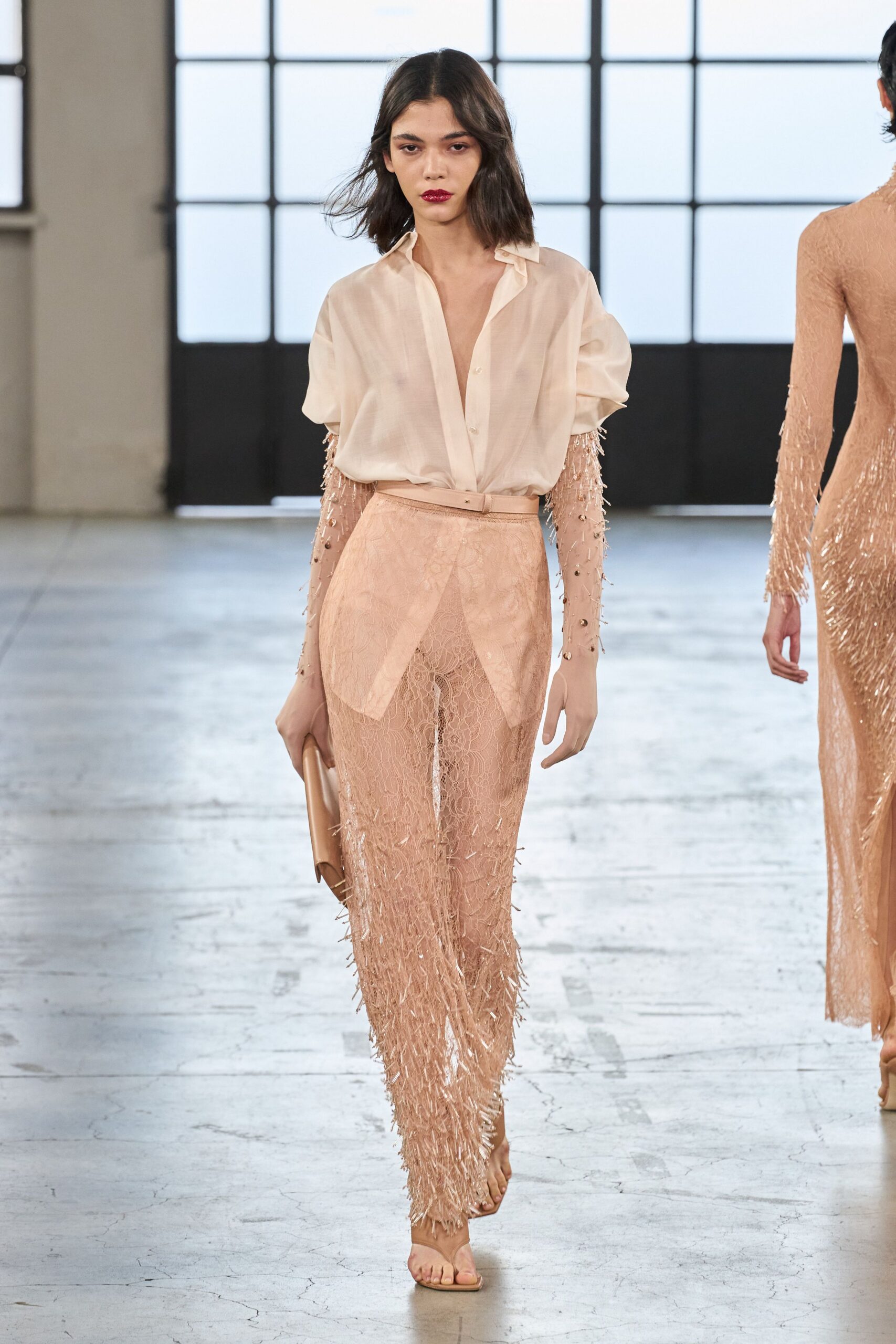 Sheer blush blouse, collar open and sleeves puffed above the elbow. Nude illusion sleeves strewn with beaded fringe. Powder lace column skirt with an apron panel over the hips. Barely there nude thong sandals. Champagne satin foldover clutch. Crossing a hotel lobby after a wedding, heels already in hand.