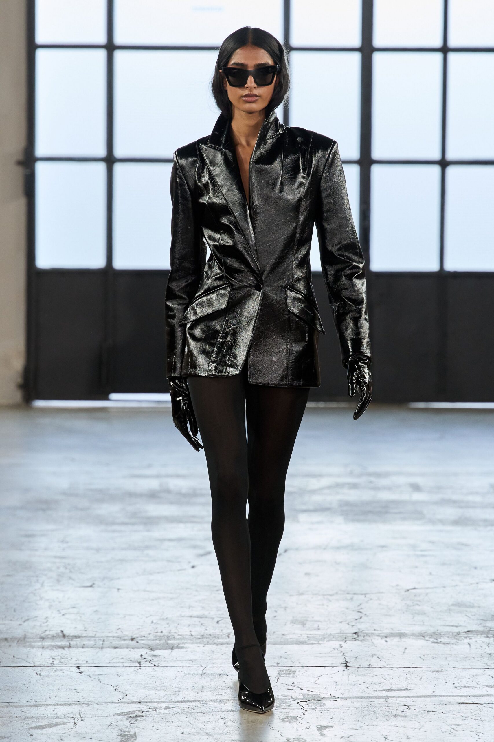 Angular black acetate frames with a heavy brow line. Black liquid-shine blazer dress, peaked collar and one low button. Second-skin patent gloves disappearing into the sleeves. Opaque black tights. Patent pumps with razor-point toes. First meeting in a glass-walled office before the heat comes on.