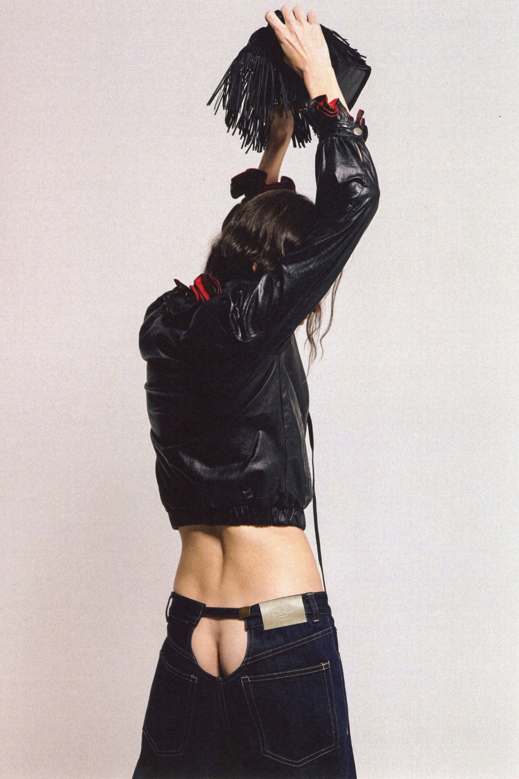 Black suede clutch with long fringe swinging over the knuckles. Black leather blouson, red ruffles peeking from collar and snapped cuffs. Dark raw-denim jeans cut away at the back, brass plaque at the waistband. Whatever you wear to miss the last train and keep dancing.