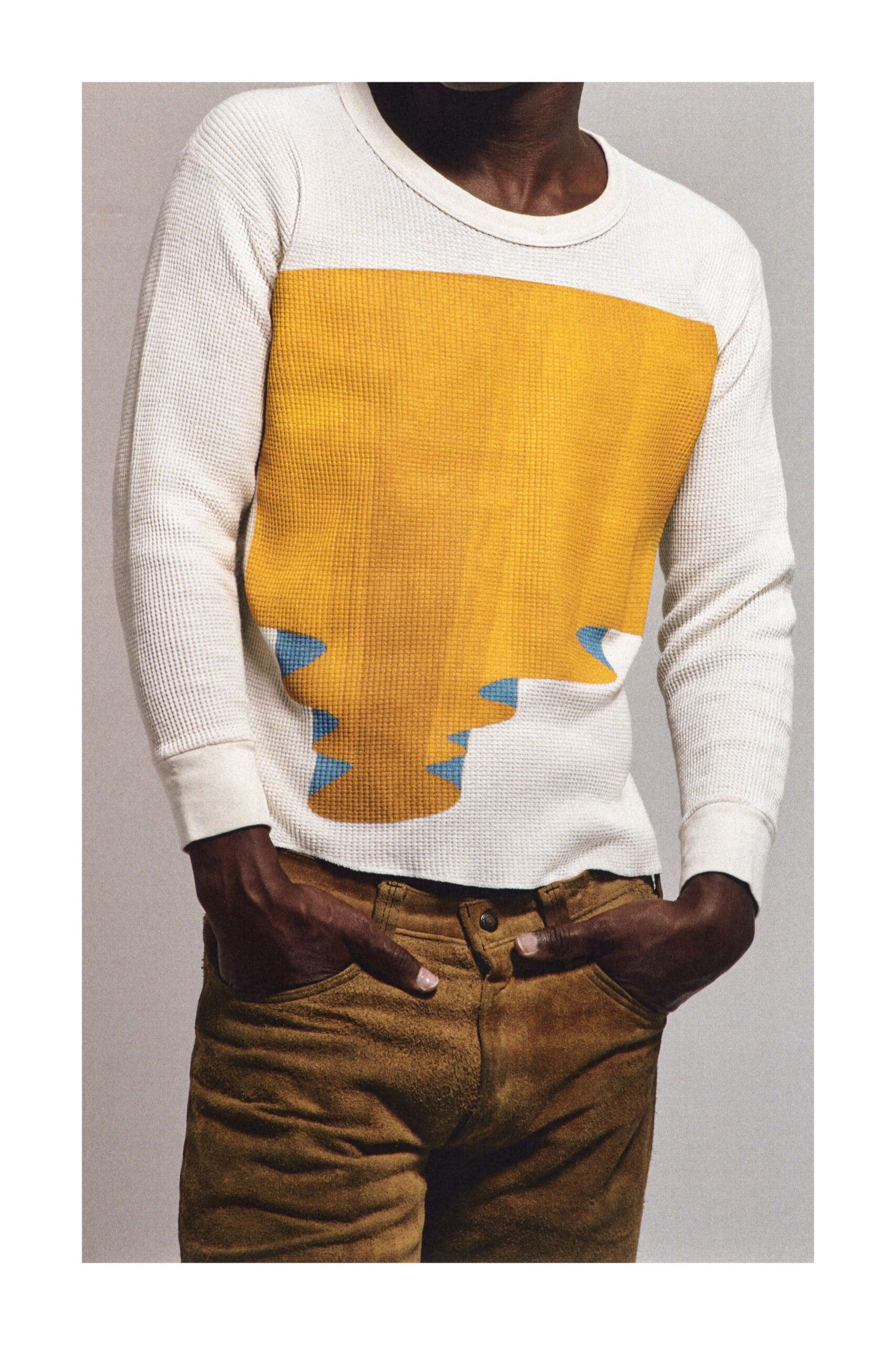 Cream waffle-knit thermal with a marigold panel dripping into sky-blue points. Tobacco suede trousers, dark rivet at the waistband. Sunday at a roadside diner after the leaves have started turning.