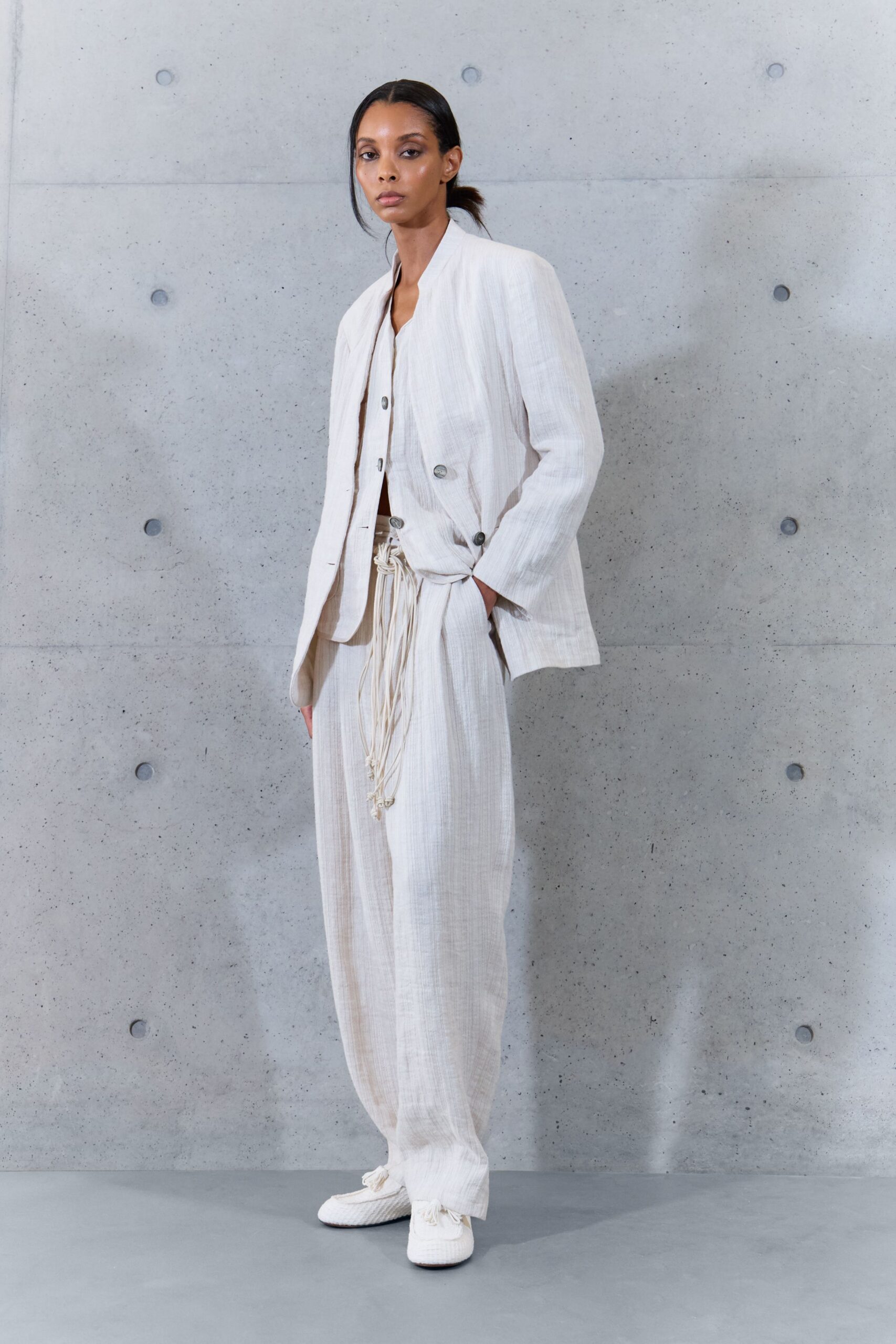 Chalk gauze jacket with a collarless edge and dark horn buttons. Matching gauze top, softly ruched where it meets the waist. Loose chalk trousers cinched with long knotted drawcords swinging at center front. White woven slip-ons with tassels brushing the floor. For the ferry crossing when the wind has turned cool off the water.