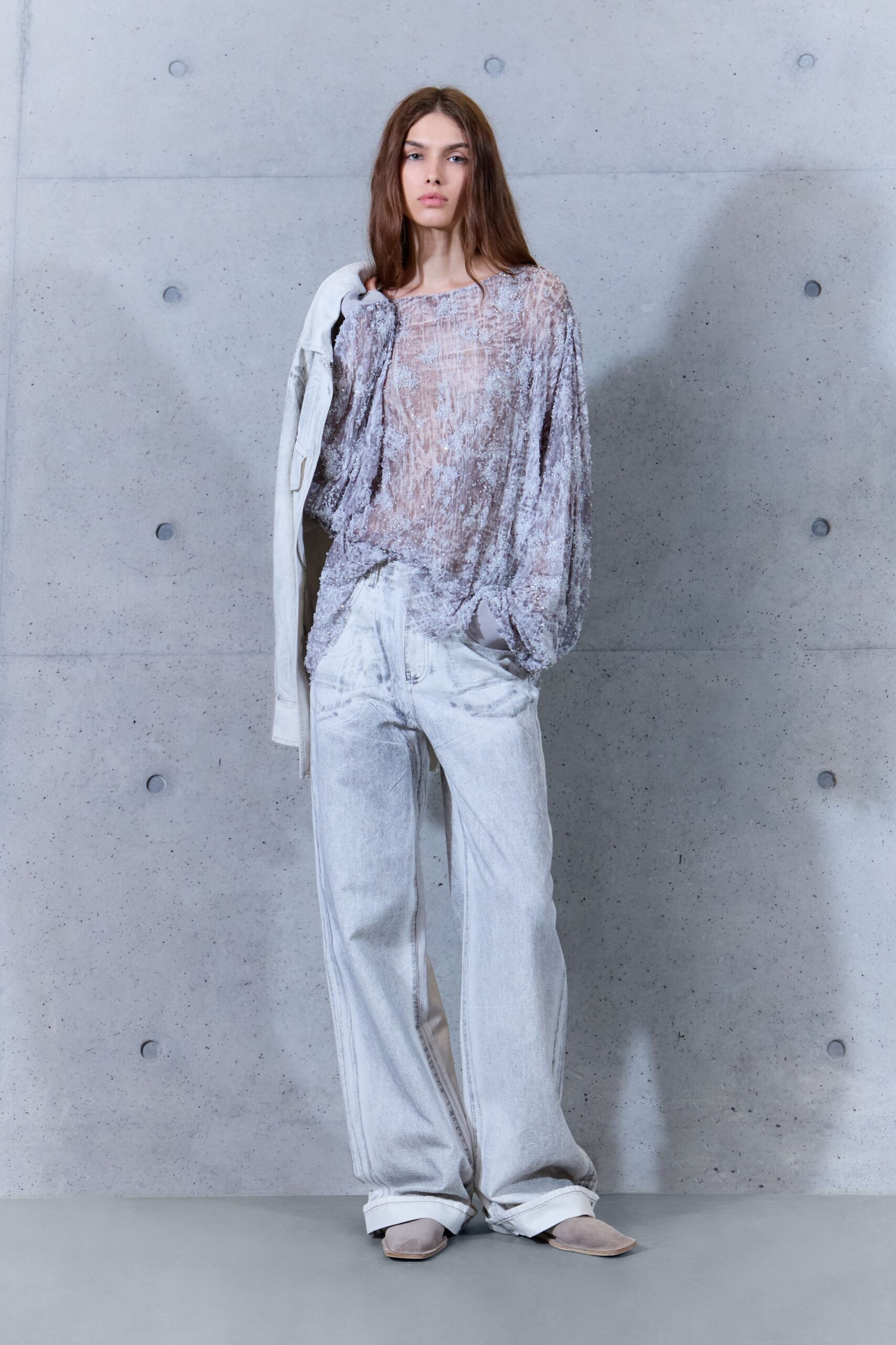 Sheer mauve blouse crusted with paillettes, neckline slipping off one shoulder. Chalk denim jacket shrugged low, hanging from one arm. Bleached wide-leg jeans with pooled cuffs and a faded whisker at the fly. Pale suede square-toe flats. Early train after the wedding, confetti still stuck in your hair.