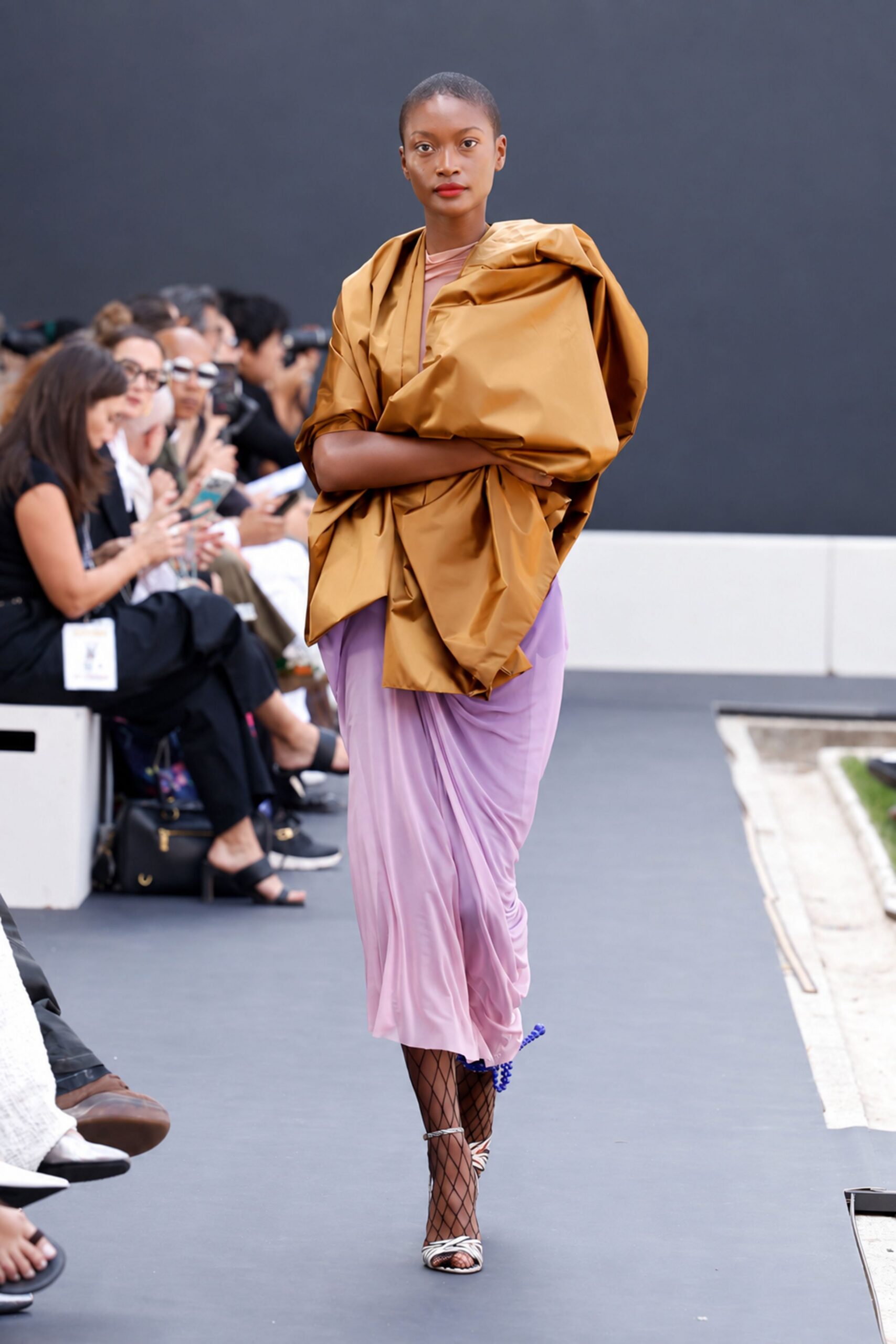 Bronze taffeta wrap, crumpled into huge origami folds around the shoulders. Lilac jersey dress, softly ruched and draped close through the hips. Black diamond-net tights. Silver cage sandals with a bright cobalt pompom at the heel. Crossing a sculpture garden after rain, carrying your coat any way it will stay.