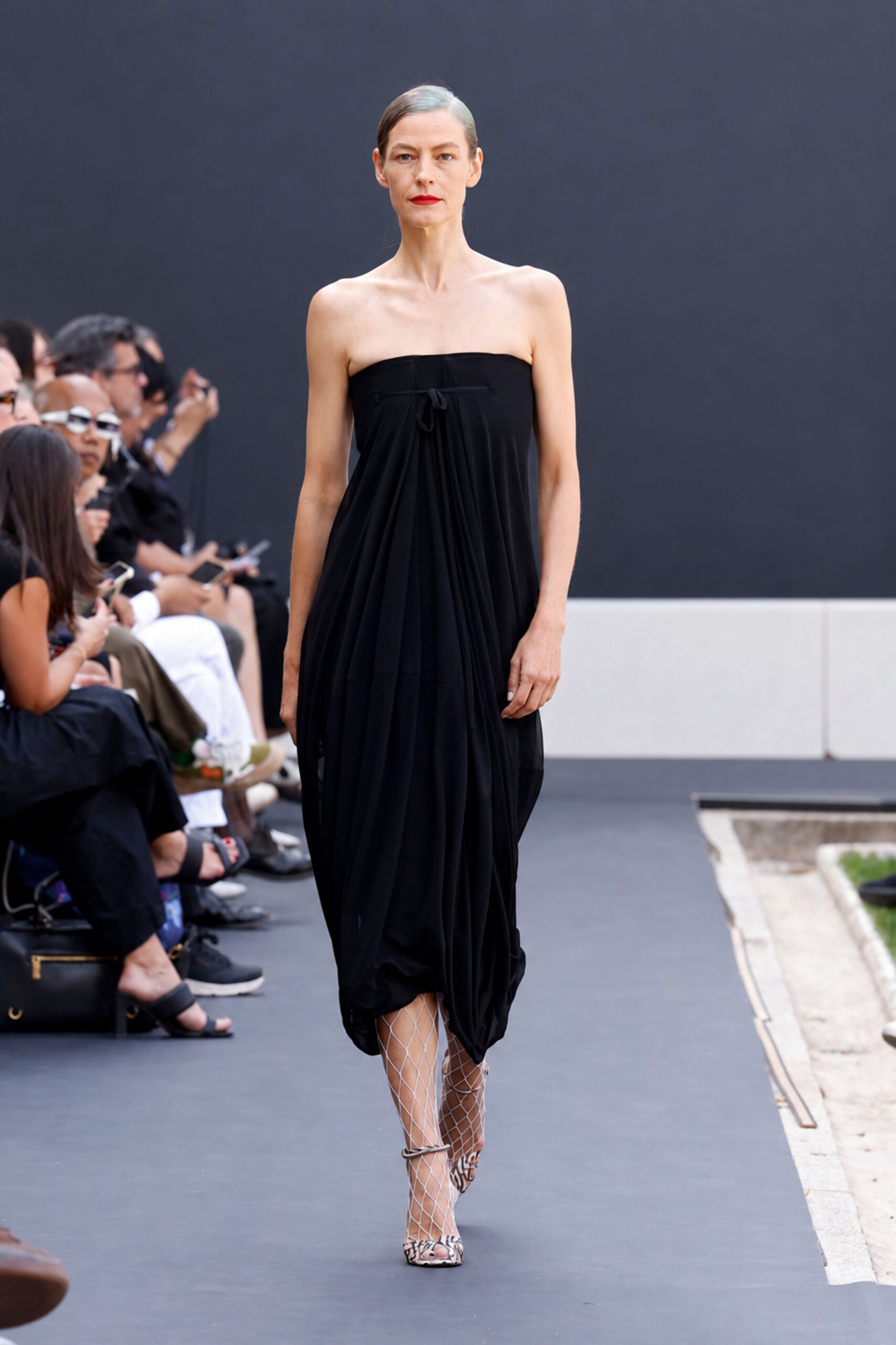 Black strapless jersey dress, softly draped from a narrow tied band. White diamond mesh climbing past the knee. Zebra peep-toe heels with thin wraparound ankle straps. Crossing a hotel courtyard before breakfast, still carrying last night's lipstick.