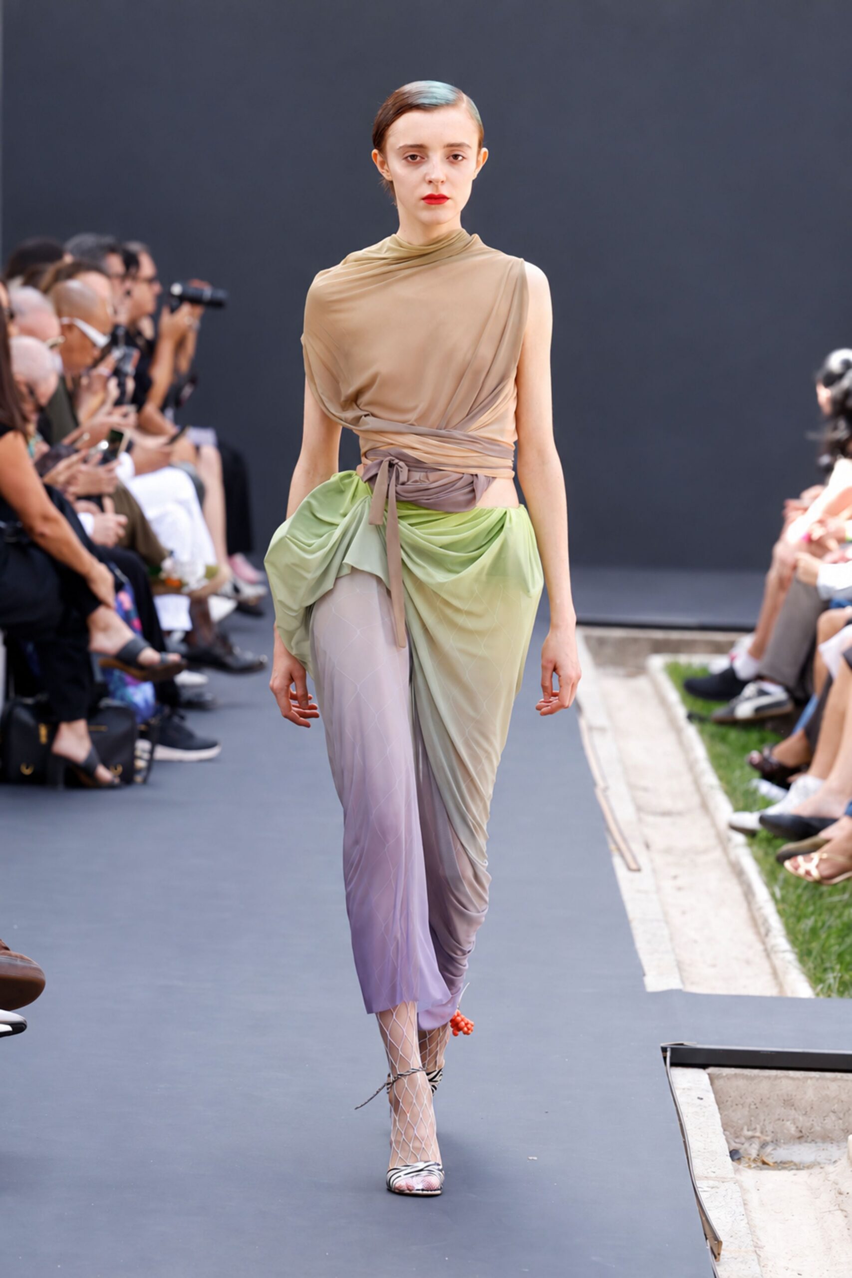 Taupe stretch-jersey top draped off one shoulder and wrapped twice at the waist. Pistachio and lilac mesh skirt ruched into heavy side swags. White diamond-net stockings. Zebra-print heels with a red bead cluster at one ankle. Walking the garden path after a wedding, shoes sinking into the lawn.