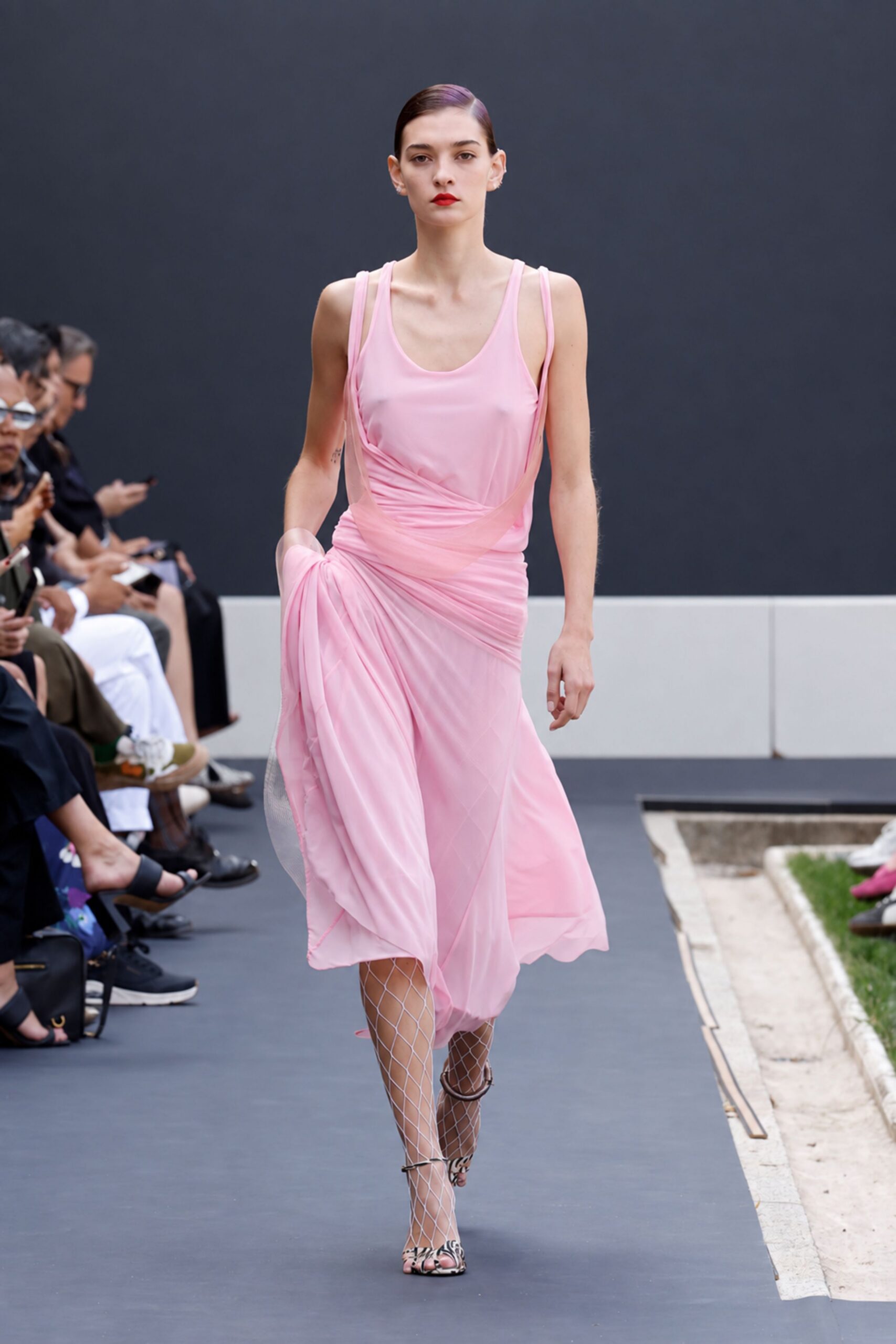 Blush chiffon slip dress, twisted and ruched low across the hips. White diamond fishnet tights. Ankle-strap heels in zebra print, toe peeking through the cage. Garden wedding after the speeches, walking back from the grass to stone.