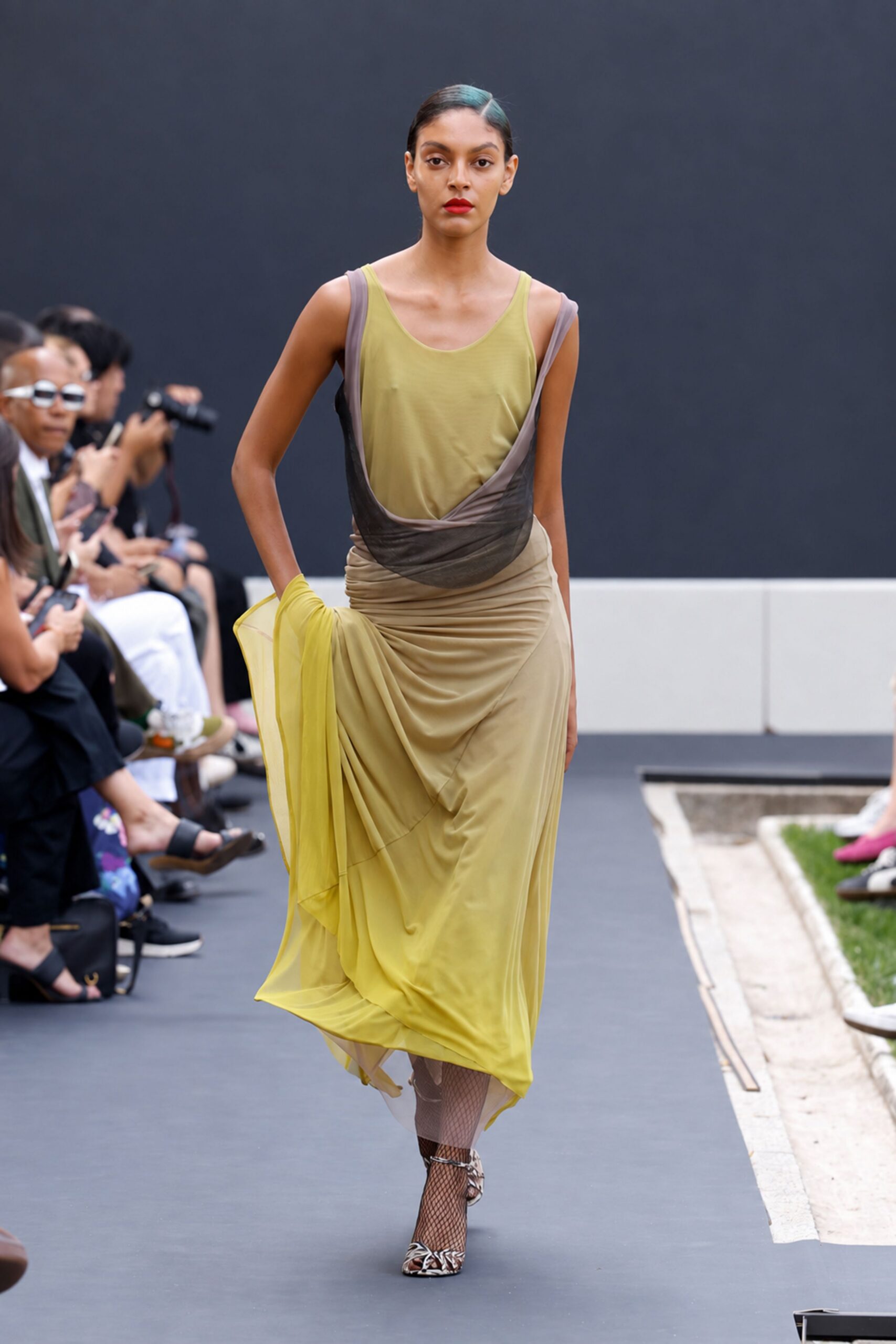 Olive jersey tank, thin straps and a wide scooped neck. Taupe mesh slip dress twisted low across the torso. Chartreuse draped skirt, ruched at the hip and pooling unevenly. Taupe fishnet stockings. Zebra-print pointed heels with ankle ties. Crossing a sculpture garden just before the storm finally breaks.