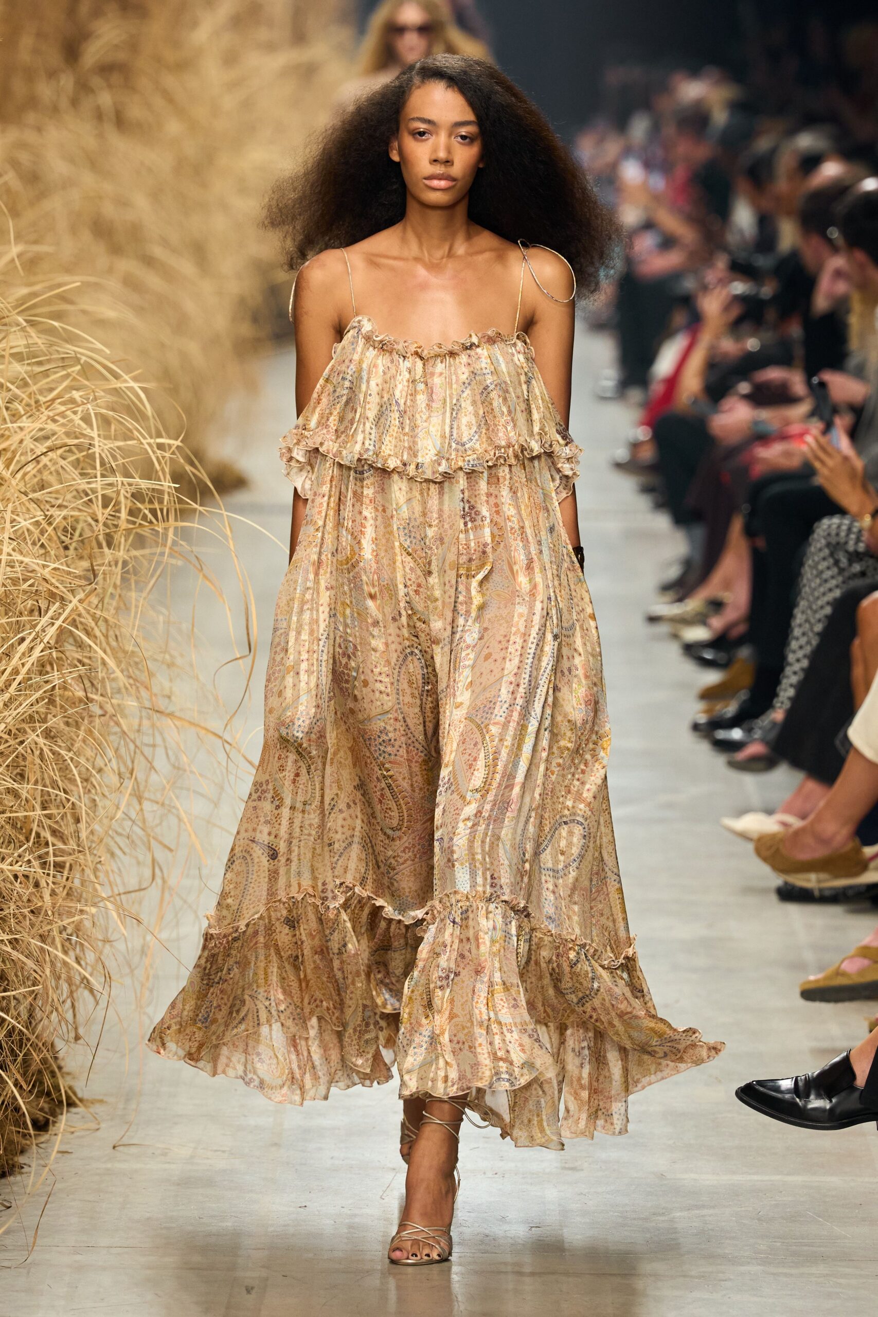 Sheer sand chiffon maxi dress in faded paisley, ruffled off-shoulder flounce. Fine metallic straps looped loose off the shoulders. Barely-there lace-up sandals in pale tan leather. Walking back from the dunes with salt drying on your collarbones.
