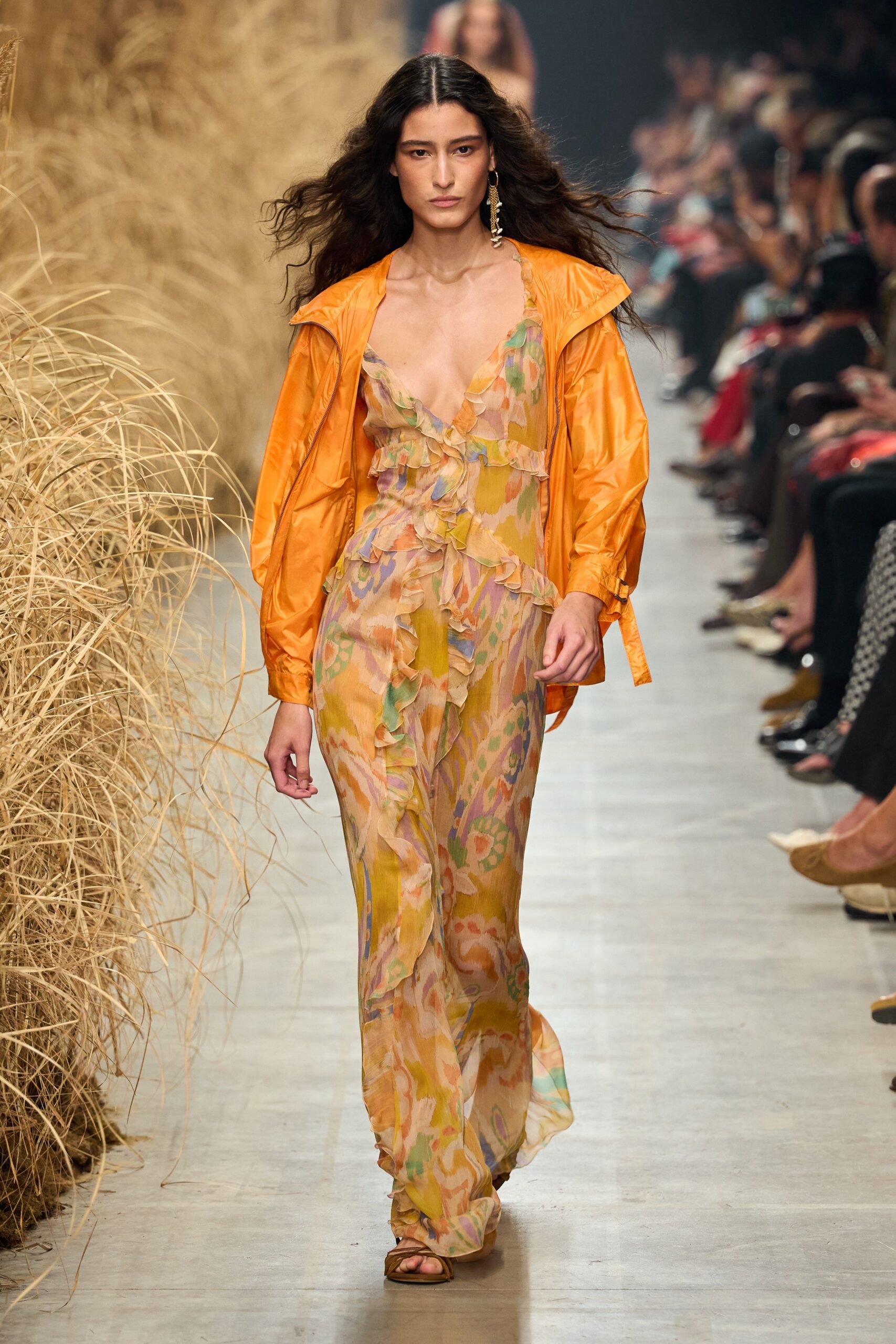 Glossy tangerine shell jacket, zip open and cuffs loosely tabbed. Sheer ankle-length dress in washed ikat tones, ruffles spiraling down the front. Single shell-drop earring. Flat tan sandals. Walking back from a beach bar with salt drying on your shoulders.