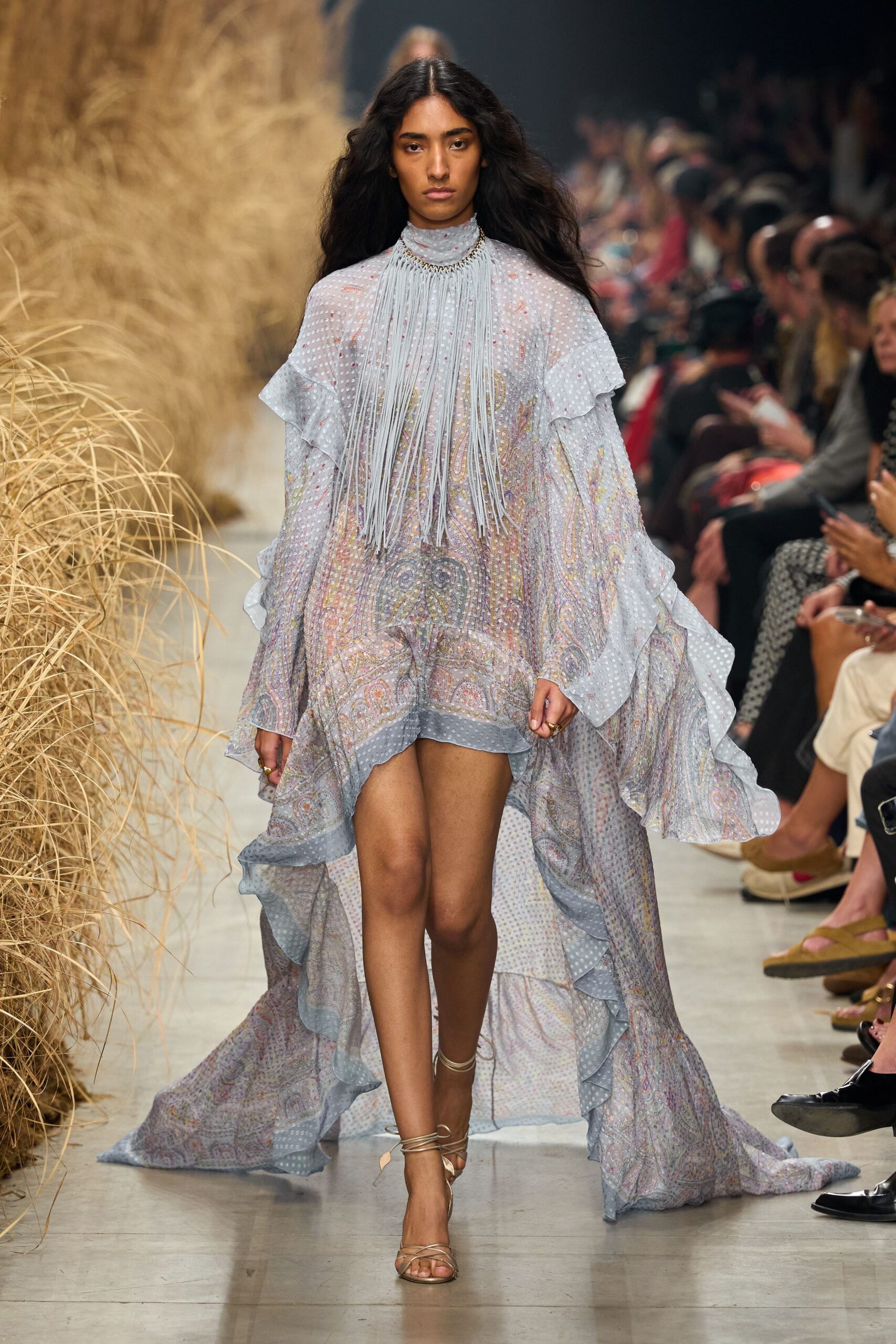 Ice-blue chiffon dress in mixed paisley and clipped-dot, with waterfall ruffles and a high-low train. Long pale fringe pouring from a chain-trim mock neck. Barely-there metallic lace-up sandals circling the ankles. Crossing a dry paddock after the wedding music has carried off on the wind.