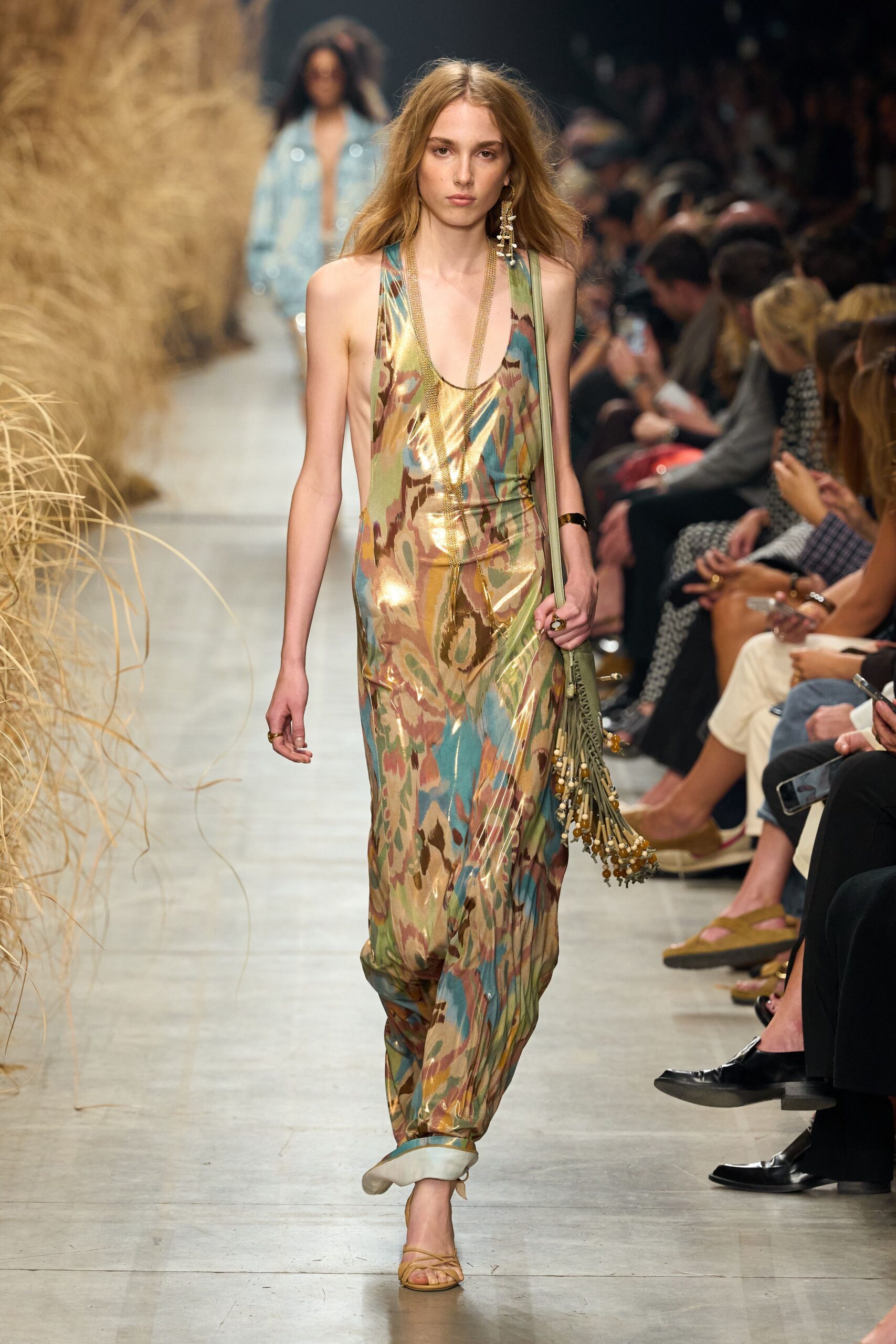 Liquid metallic slip dress in washed ikat, cut low at the sides. Long gold mesh chain doubled down the chest. Single shell-cluster drop earring brushing the shoulder. Sage shoulder bag with swinging bead tassels. Barely there leather sandals. Walking back from the beach bar with salt drying on your collarbones.