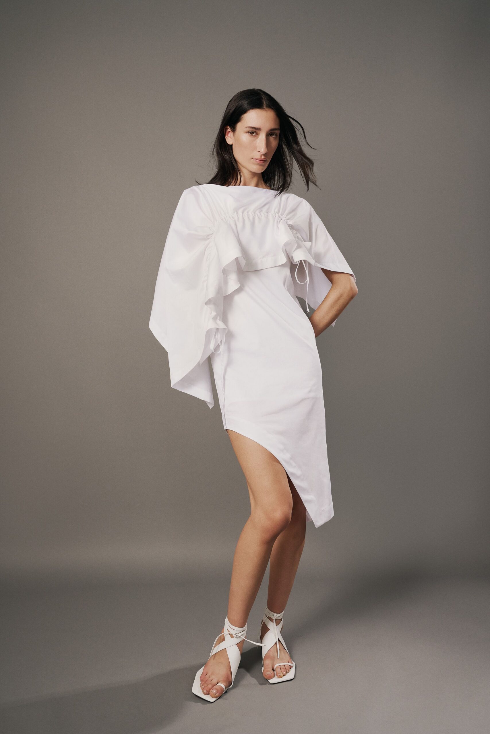 White cotton dress with ruched chest ruffle and an angled hem. White square-toe sandals laced high around the ankle. Courthouse steps in summer, papers folded in a tote.