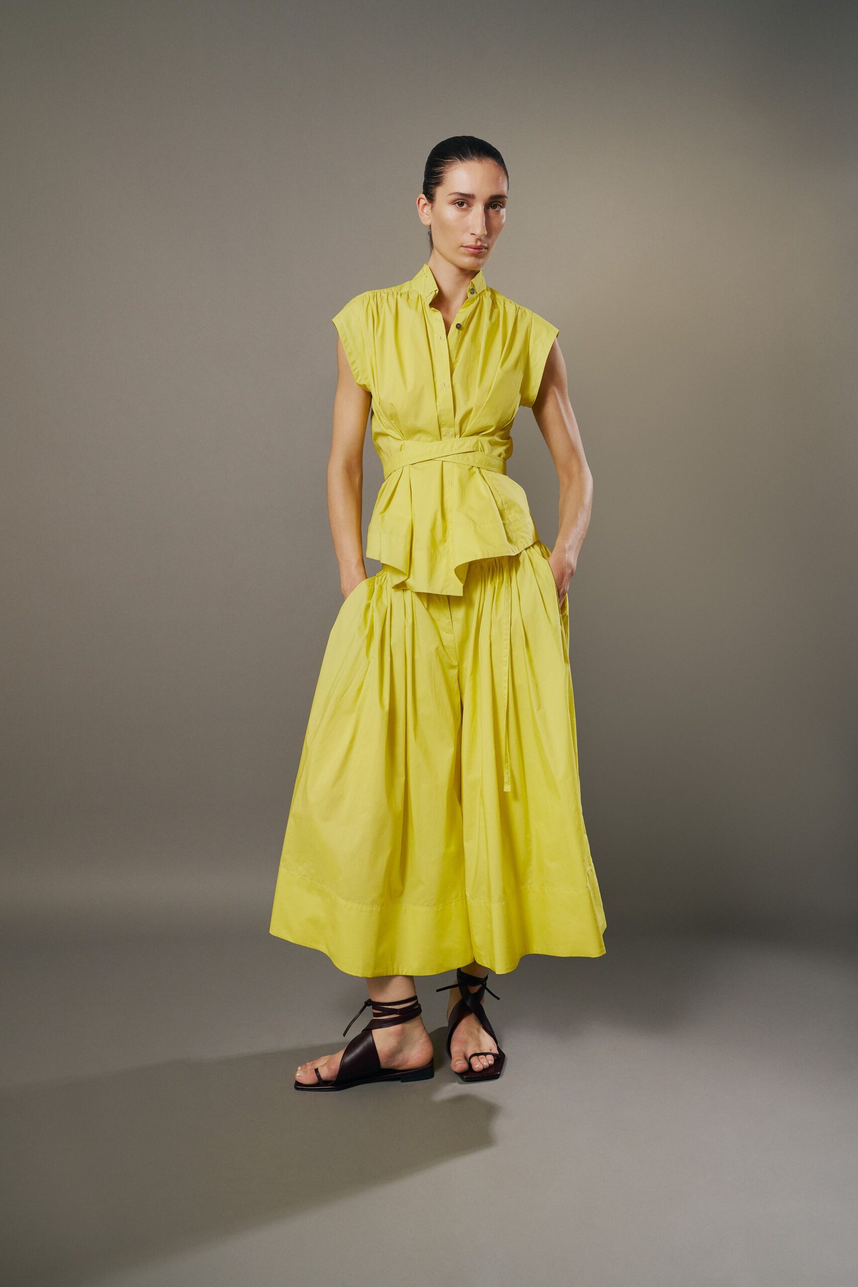 Citron poplin top with cap sleeves and a wrapped self-belt waist. Matching full skirt, densely gathered with a long drawcord hanging front. Dark brown leather sandals laced high around the ankles. For crossing a sunblown courtyard after the hotel pool has emptied.