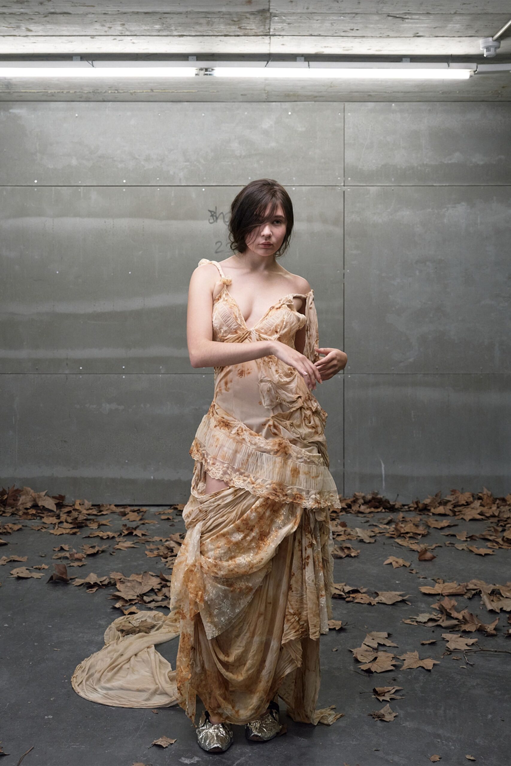 Tea-stained ivory slip dress, ruched cups and torn lace tiers sagging sideways. Crumpled silver shoes peeking from the pooled hem. Under strip lights after the reception, leaves blown into the loading bay.