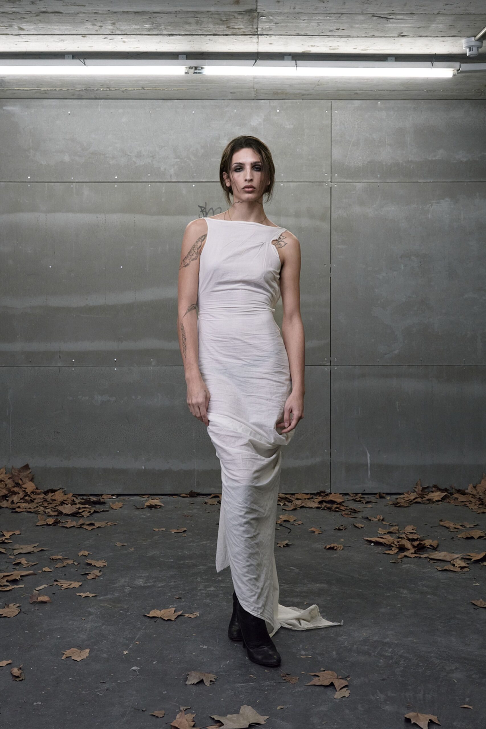 Ivory jersey column dress, asymmetrical neckline and ruched twist at one shoulder. Black leather ankle boots, squared toes peeking under the dragging hem. Walking across a car park scattered with wet plane-tree leaves.