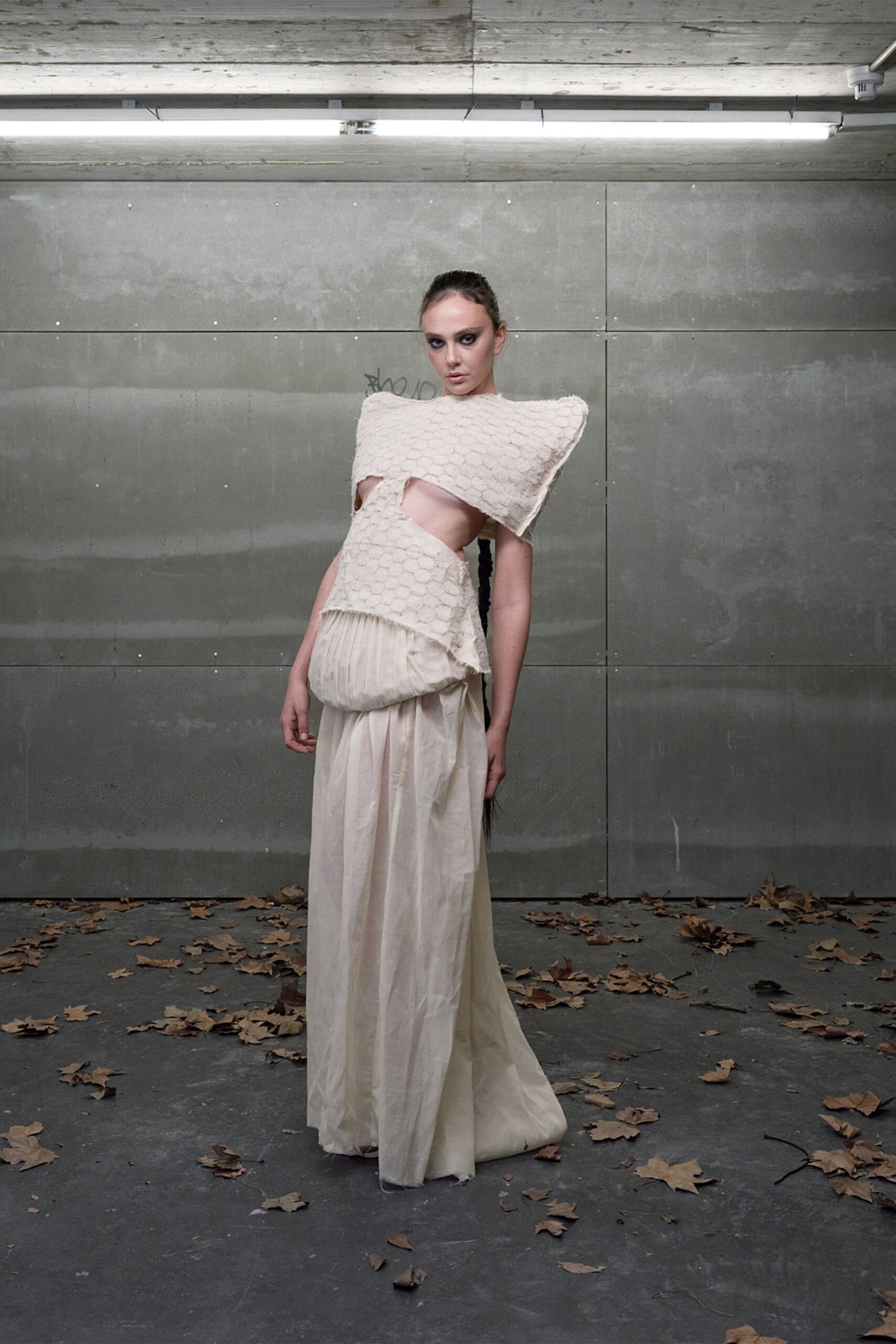 Ivory honeycomb-textured top with squared wings jutting past the shoulders. Milk-white gauze skirt, drop waist gathered into a bulbous pouch front. Under strip lights in a concrete loading bay after the leaves blew in.
