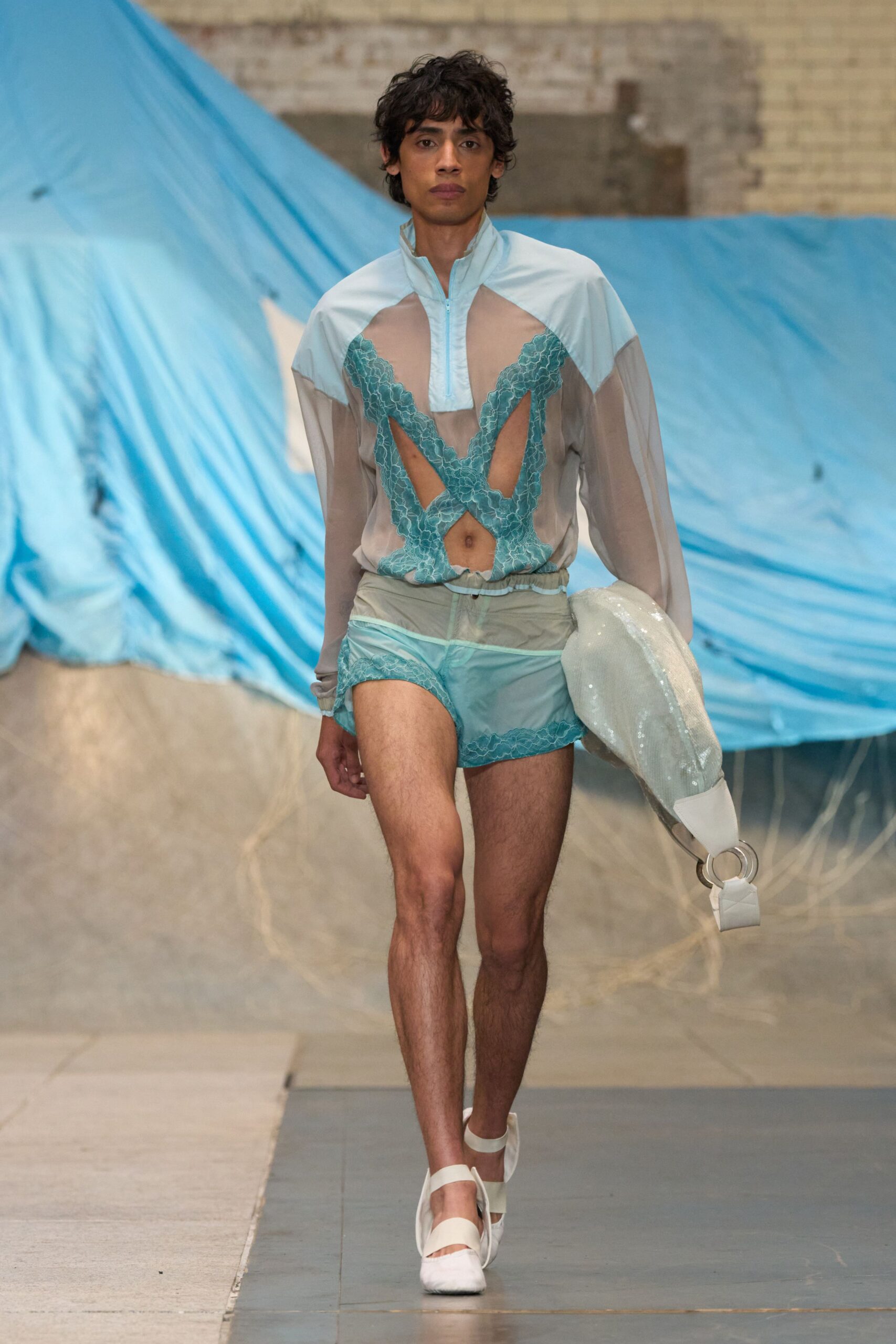 Sheer dove-grey top with aqua lace appliqué carving deep front cutouts. Matching translucent track shorts, lace edging skimming the leg opening. White sequined tubular bag with a large silver ring handle. White flats with broad elastic straps. Walking from a lido changing room with chlorine still drying on your skin.