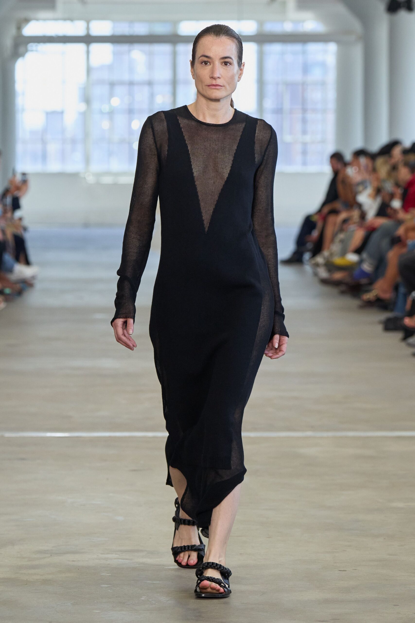 Black gauze knit top, long sleeves ending in thumbhole-like hand slits. Black sleeveless knit dress with a plunging V framing a sheer chest panel. Flat black sandals with puffed tubular straps across the toes. Walking home from a gallery opening before the heat leaves the pavement.