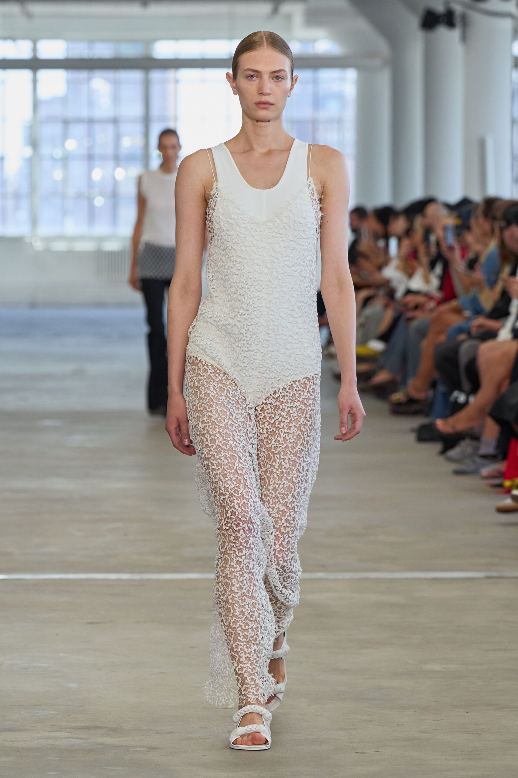 Ivory scoop-neck slip dress, bodice densely tufted into soft nubby rows. Sheer white floral lace trousers falling from a pointed handkerchief underlayer. White sandals with thick braided straps. Walking the boardwalk before noon, swimsuit still damp under borrowed clothes.