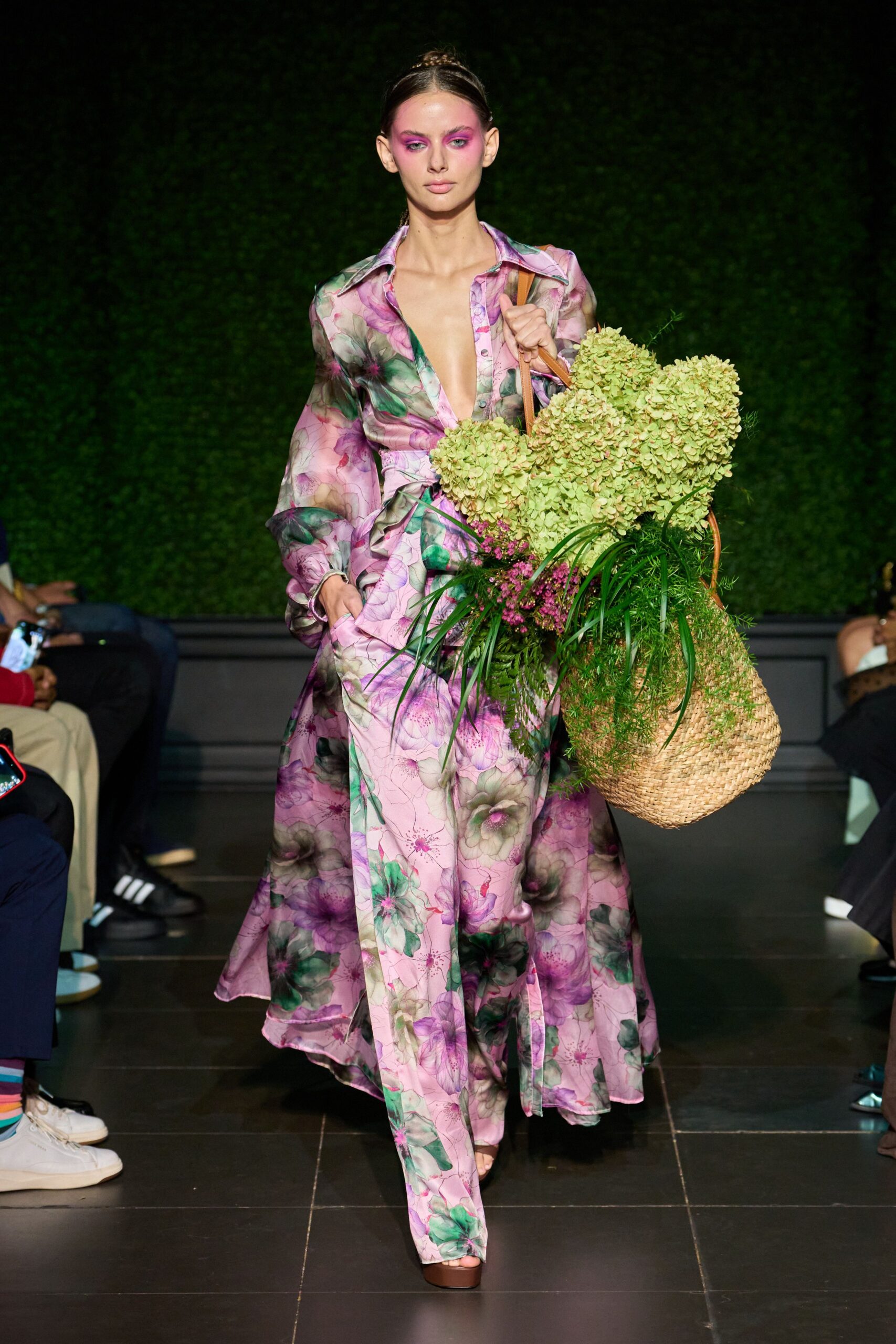 Sheer pink floral blouse, unbuttoned deep with loose bishop sleeves. Matching wrap skirt falling to the floor, tie end trailing long. Brown platforms peeking from the hem. Woven straw tote stuffed with pale hydrangea heads and fern. Walking home from the flower market before the stems start dripping.