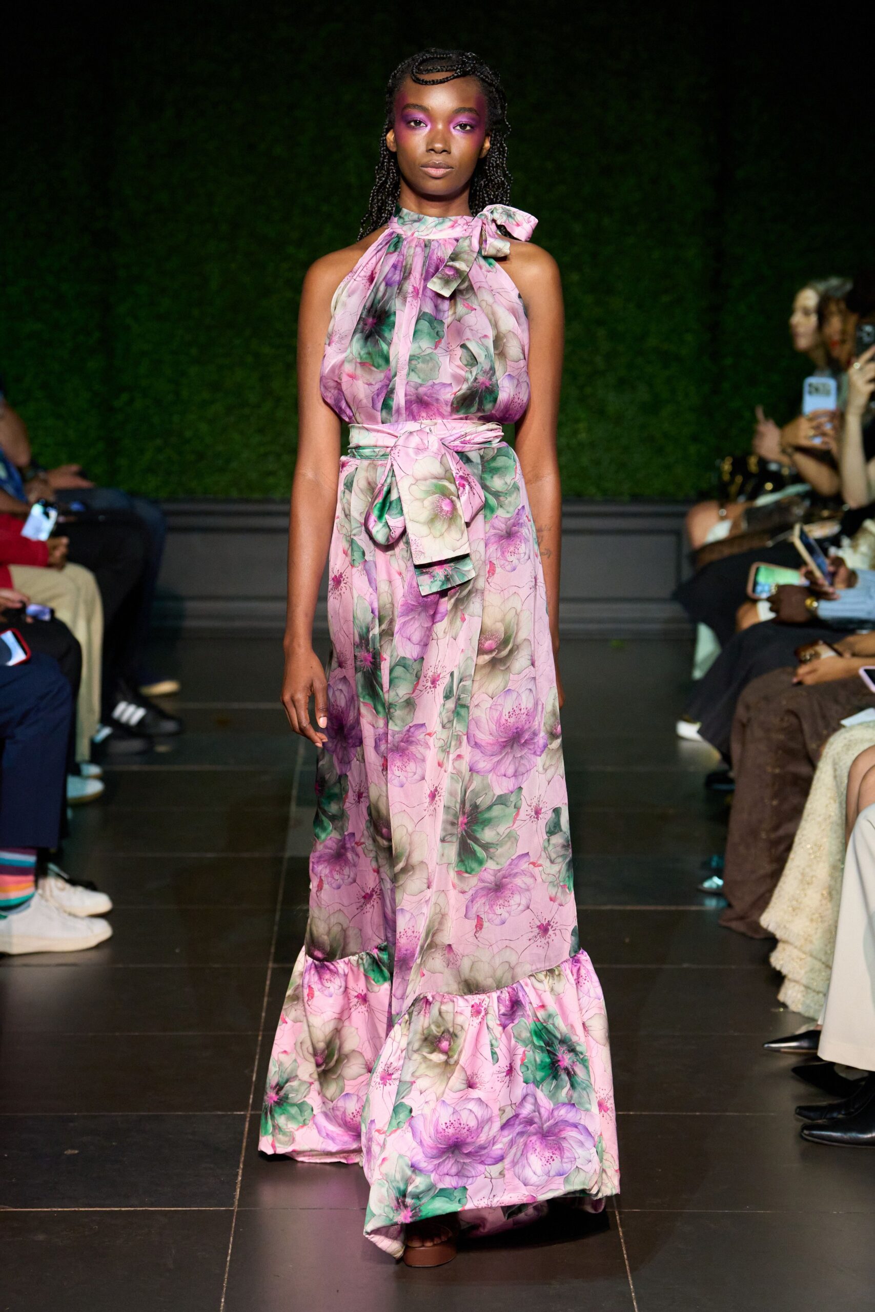 Pink floral chiffon halter dress with a neck bow and dropped ruffle hem. Matching self-tie sash, one end hanging longer at the waist. Brown platform sandals just peeking under the floor-length skirt. Garden wedding reception after the sun has gone down.