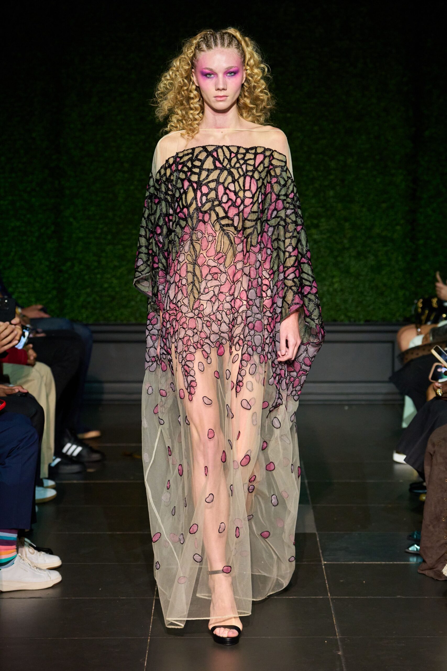Sheer nude tulle caftan with black corded appliqué blooming into mauve petals. Black ankle-strap sandals with a plain narrow toe band. Walking into a conservatory wedding after the sun has already dropped.