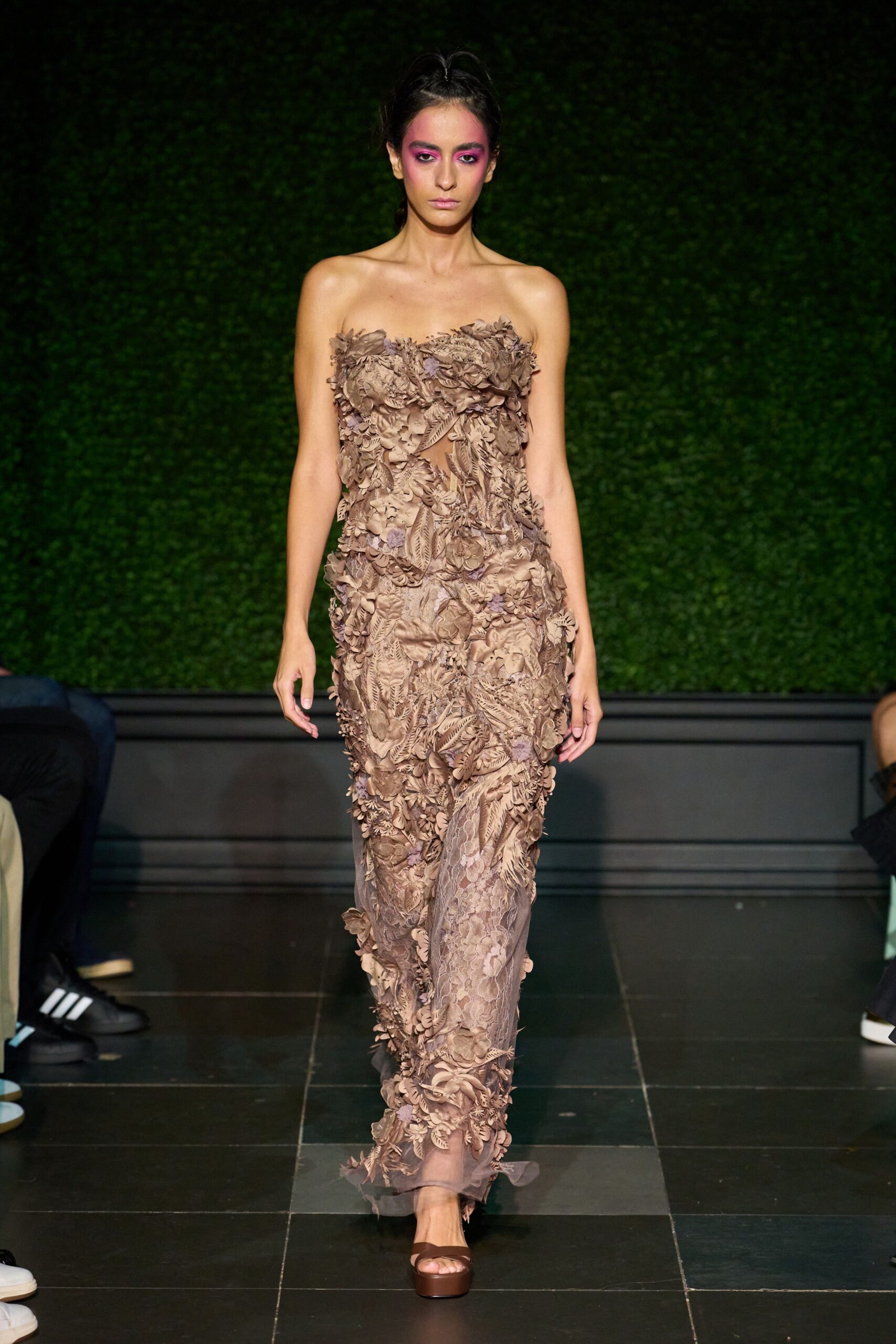 Strapless taupe column gown buried under appliqued leaves and petal clusters. Chocolate platform slides with a blunt square sole. Garden wedding after rain, hem drinking from the flagstones.