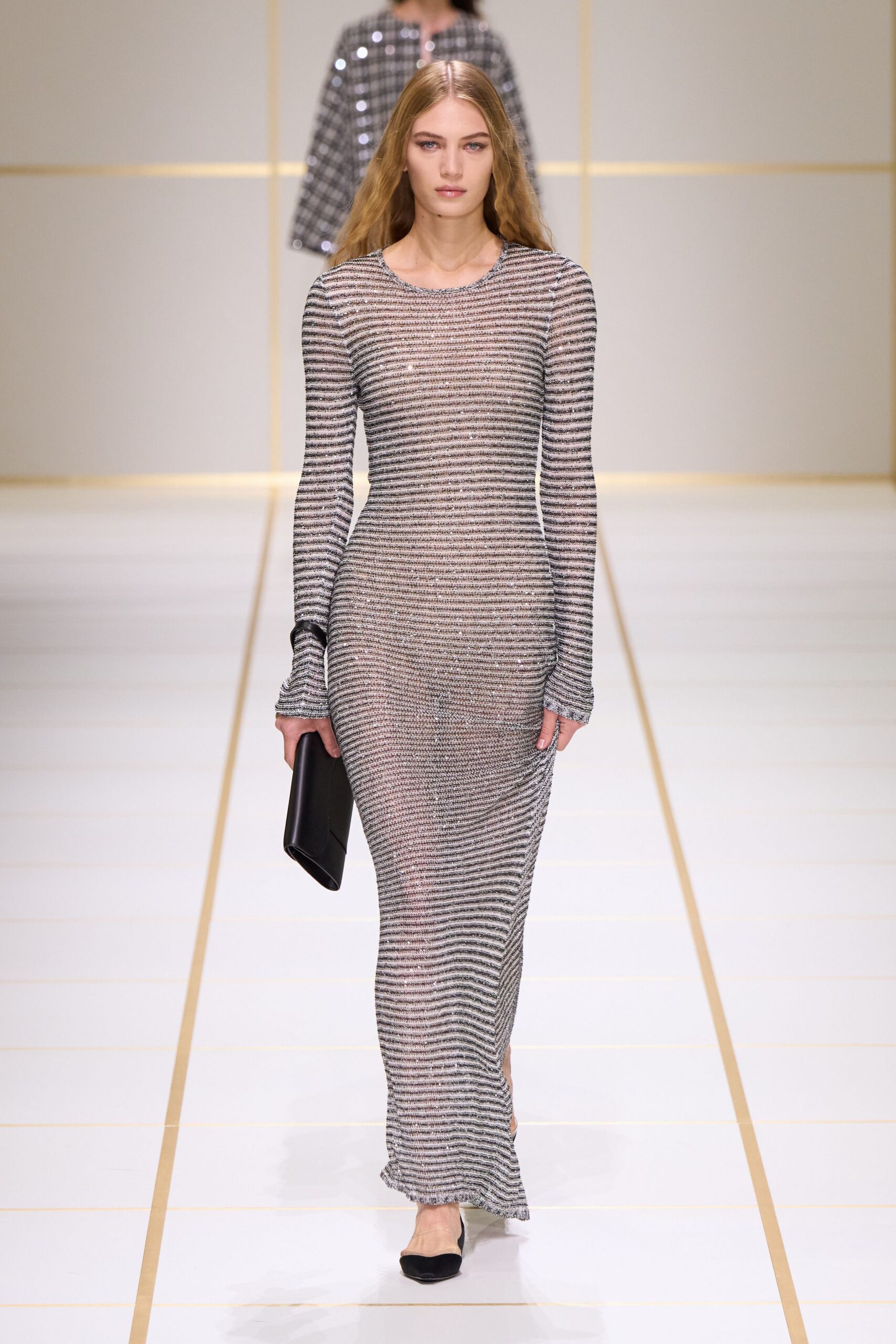 Fine striped knit column dress, silver flecks catching along the scooped neckline. Matte black foldover clutch tucked flat against the thigh. Black pointed flats with pale mesh vamps. Hotel corridor carpet gone quiet after the wedding finally ended.
