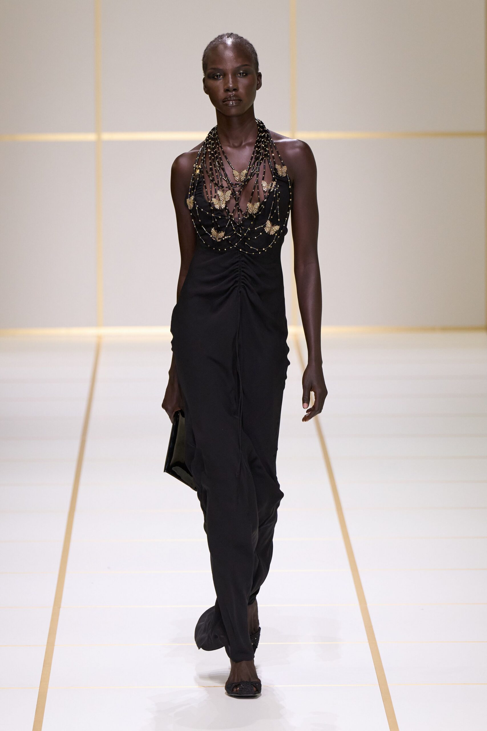 Cascading black bead strands dotted with small gold shell plaques. Black halter gown, ruched down the center and pooling at the feet. Flat black clutch tucked tight against the thigh. Black peep-toe mules with glittered fronts. For the hotel atrium after midnight, still carrying sand in your shoes.