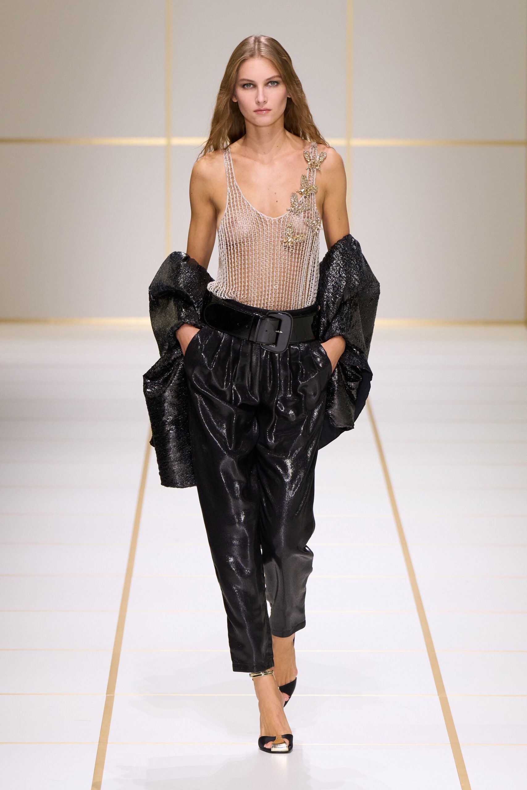 Sheer silver-beaded tank, one strap climbed by clustered crystal leaves. Black crinkled lamé wrap slipping off both arms. Inky coated trousers, softly pleated into a wide glossy belt. Black peep-toe mules with a gold-capped vamp. Crossing a hotel atrium after midnight with the room key missing.