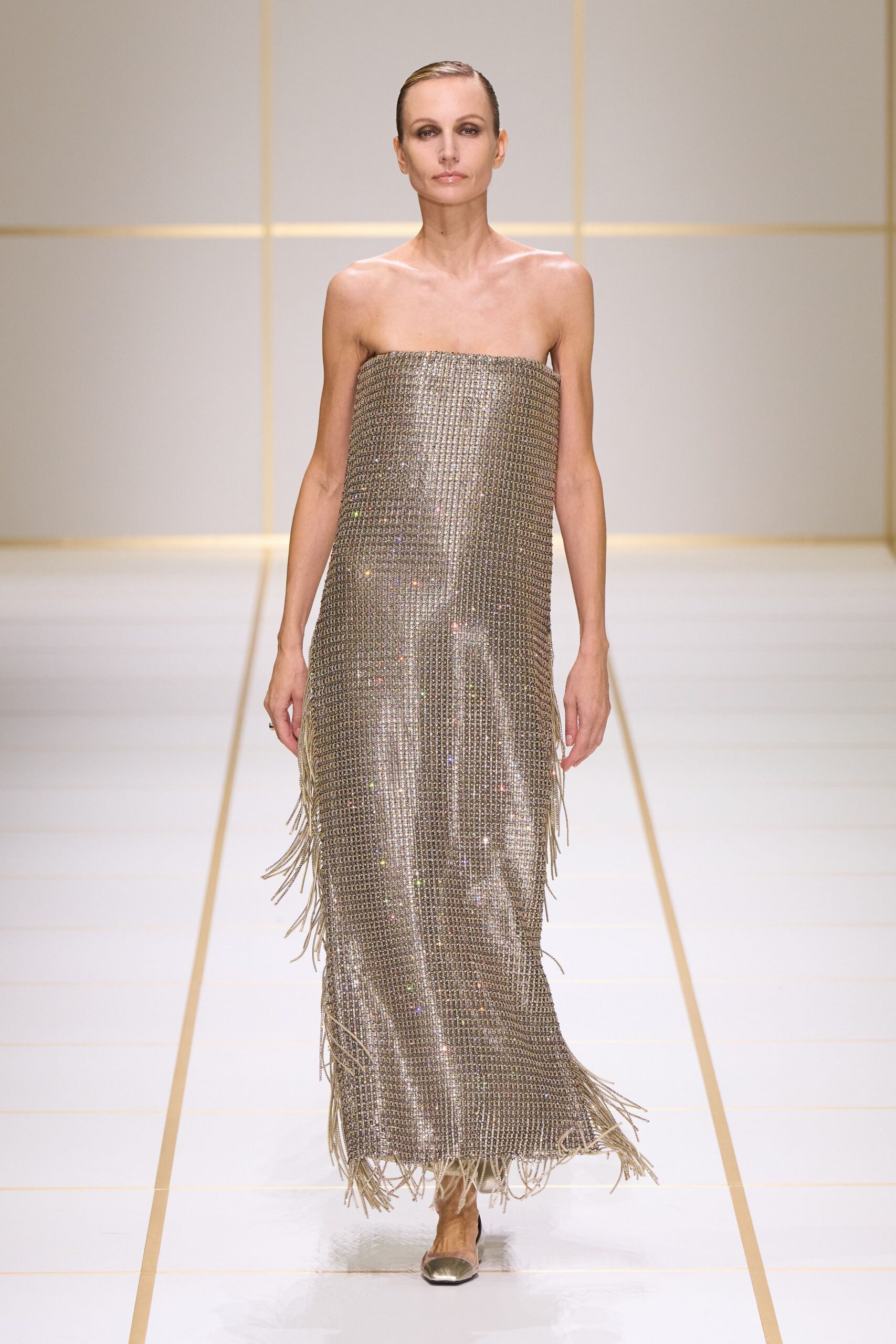 Strapless column dress in silver crystal mesh, fringe shaking from side seams and hem. Silver pumps with mirrored pointed toes. Crossing a hotel ballroom after the band has packed up.