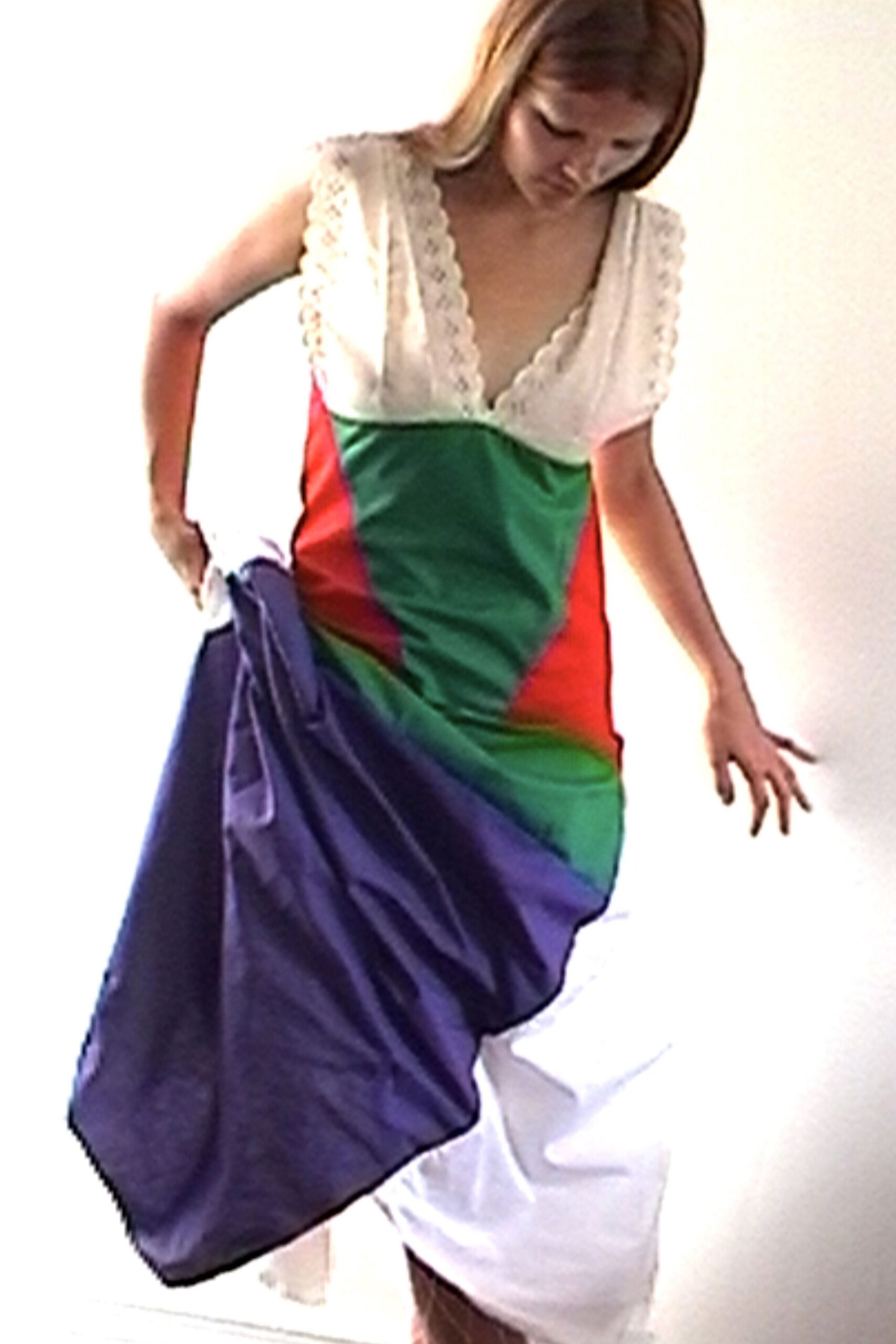Deep V dress with scalloped white lace cap sleeves and bodice. Green and red jersey spiraling into a heavy violet drape. White hem peeking out in a twisted, uneven sweep. Crossing a bare apartment with one curtain still not hung.