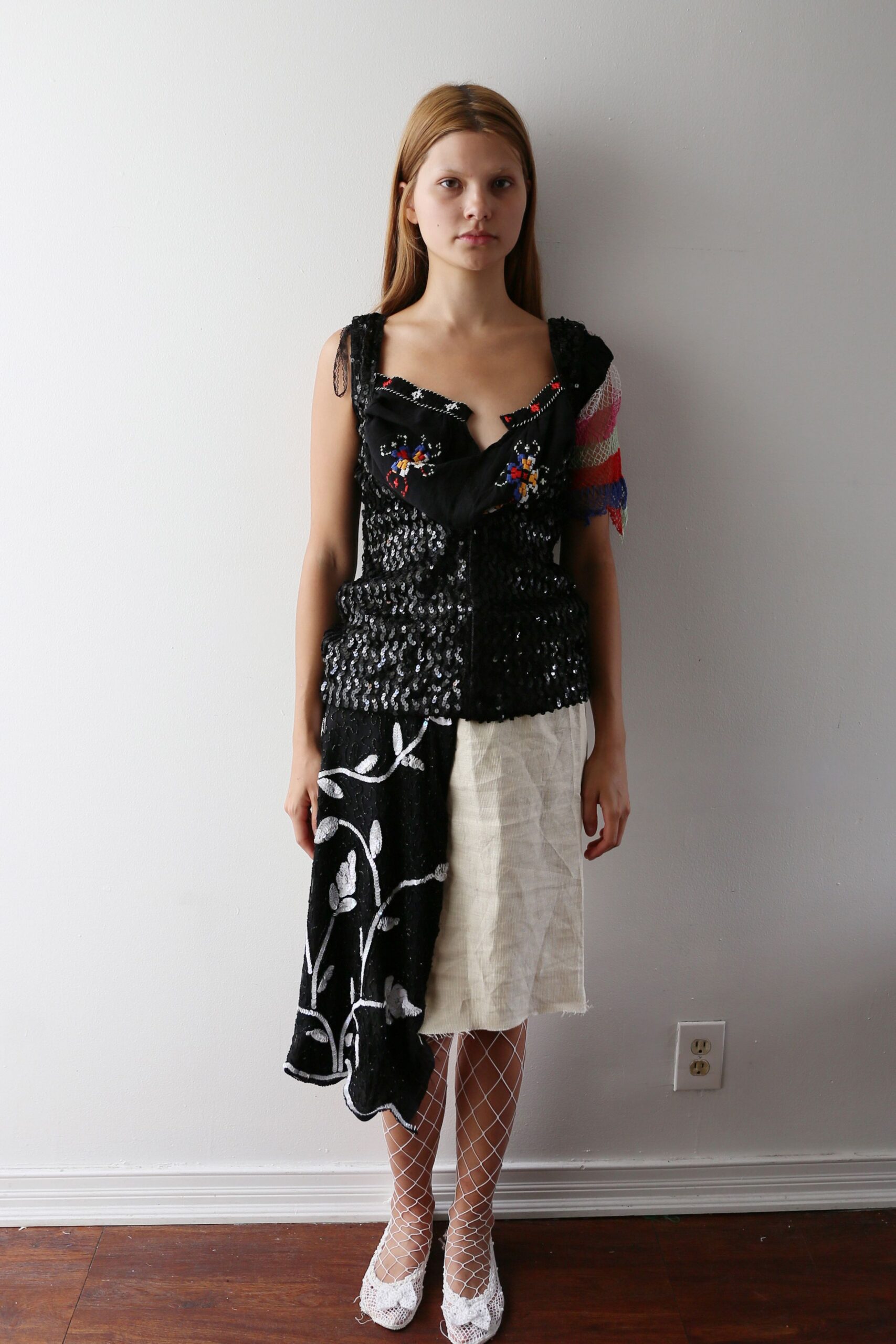 Black sequined top with a folded floral scarf neckline. Single net sleeve striped pink, white, red and blue. Asymmetrical skirt, one half black vine embroidery, one half raw linen. White diamond fishnets. White lace flats, bows fraying at the toes. Morning after a community hall recital, still half in costume.