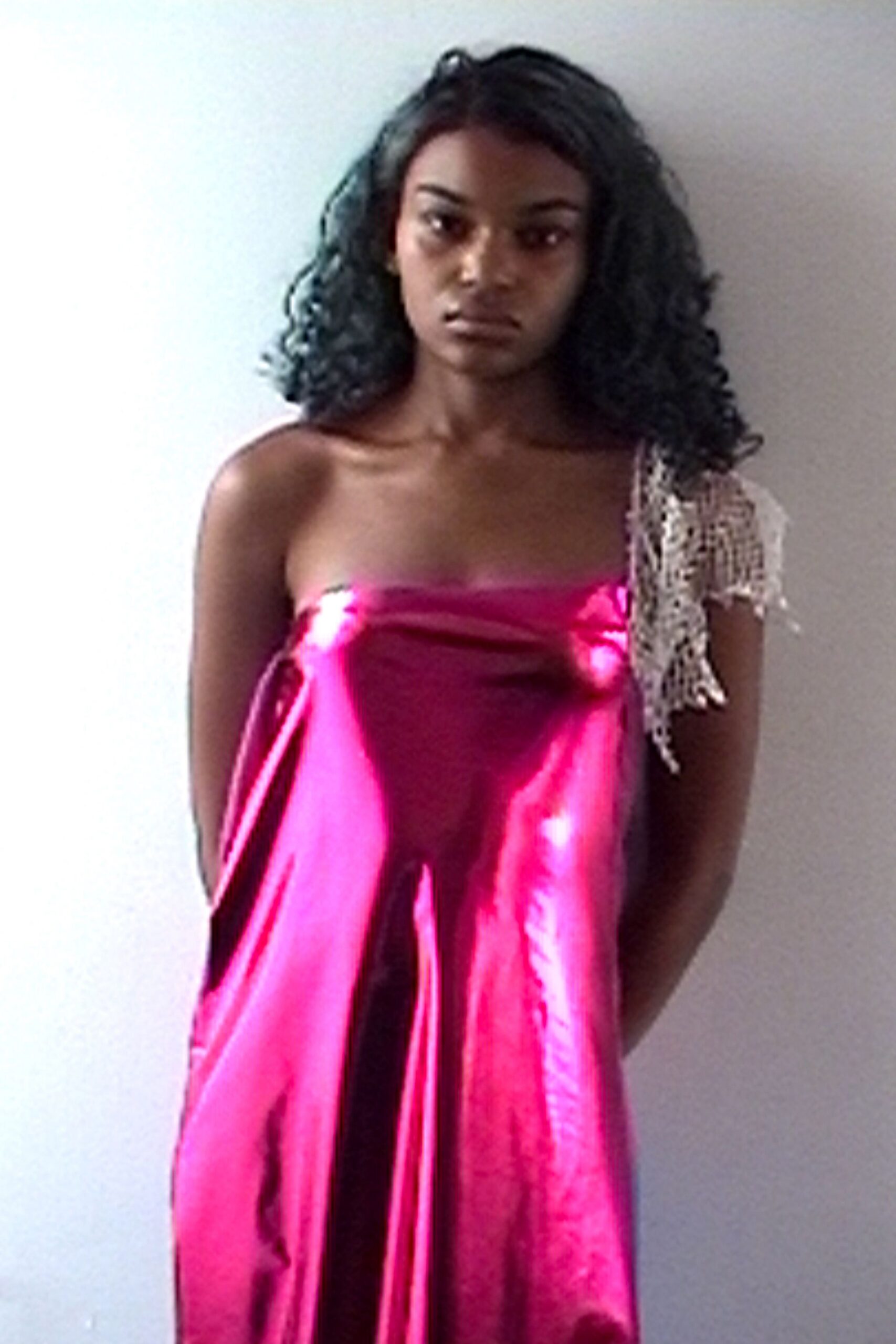 Strapless fuchsia satin column dress, cut loose with liquid vertical folds. Ivory open-knit shoulder scarf, fringe trailing from one bare arm. Standing in the patch of sun by a hotel stairwell after the wedding emptied out.