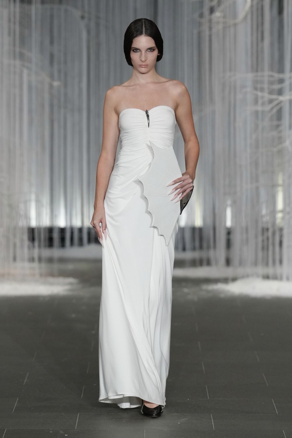 Strapless white jersey gown, ruched through the torso with a batwing side panel. Black patent pumps with a narrow pointed toe. Registry office stairs, bouquet paper going soft in your hands.