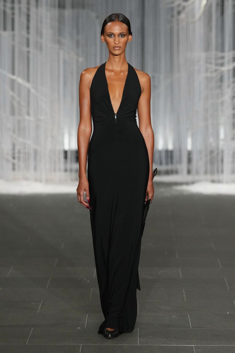 Black halter column gown in fluid jersey, plunging to a tiny silver zip pull. Slim black clutch tucked flat against the hip. Black pumps with a faintly mirrored toe cap. Whatever you wear to cross a hotel lobby after midnight, keycard in hand.