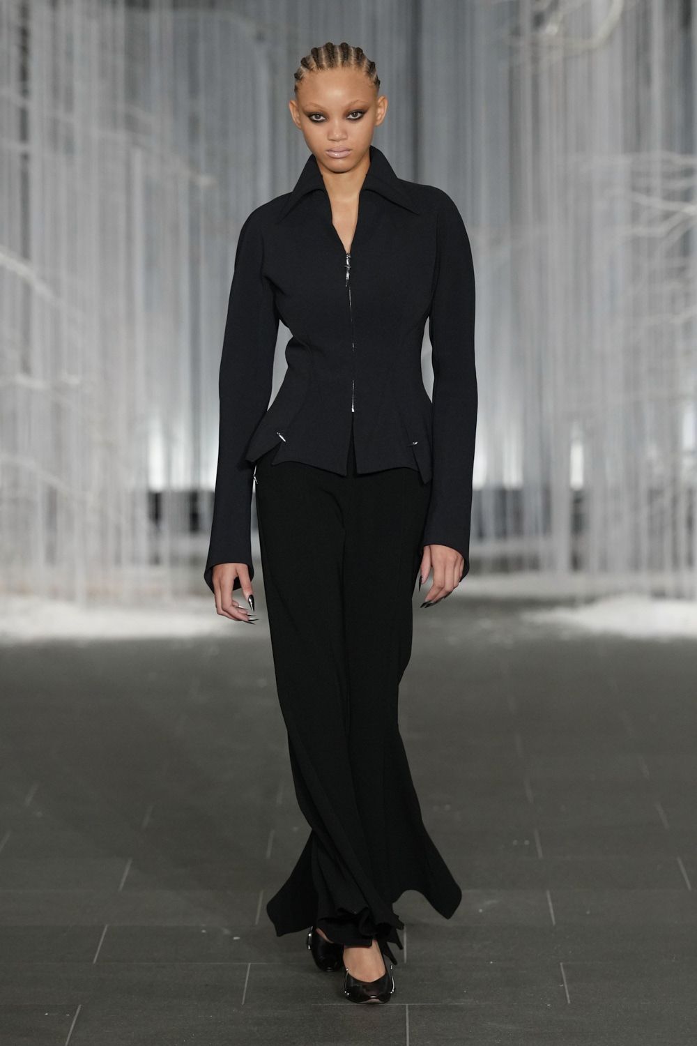 Black zip-front jacket, knife-sharp collar and peplum points over the hips. Black flared trousers breaking into a soft puddle at the hem. Black pumps with a square, light-catching metal toe cap. For crossing a hotel lobby before sunrise with your room key in hand.