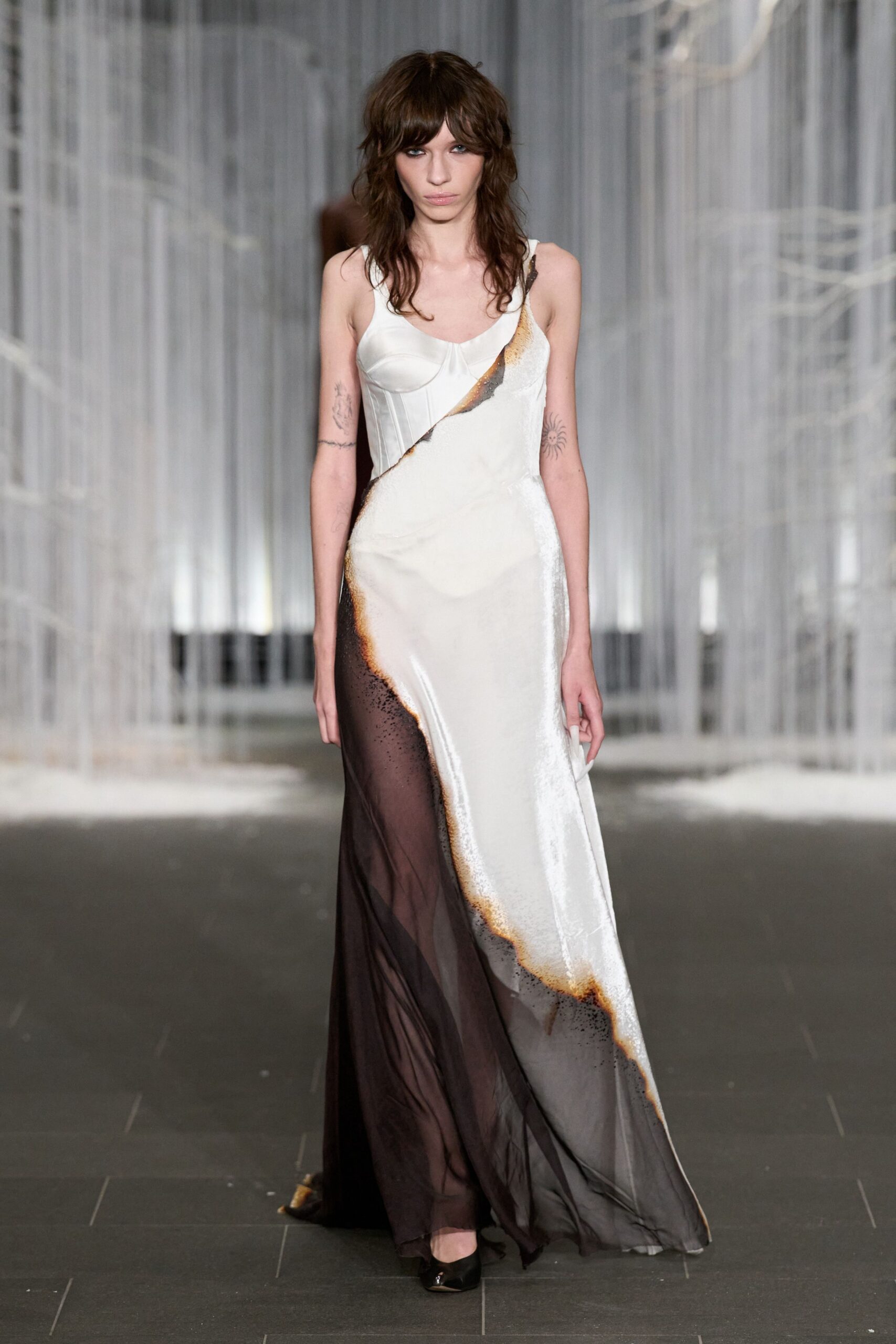 Bias-cut ivory satin gown with corset seaming and singed-looking ombre edges. Smoke-brown sheer chiffon falling from the hip in a trailing layer. Black pointed pumps, one toe catching the light. Whatever you wear to read the last page by a hotel window before dawn.