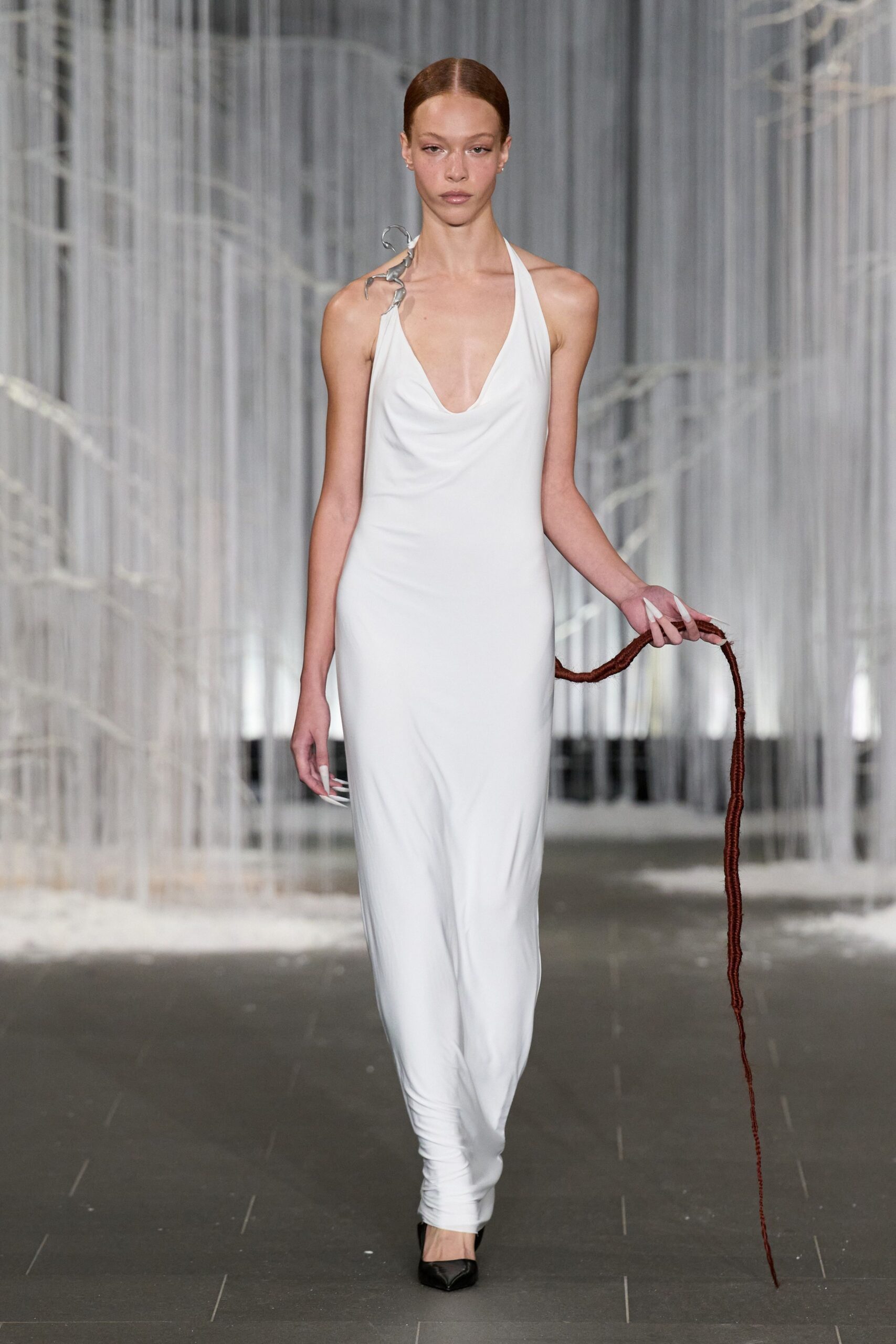 White halter jersey gown with a liquid cowl and ruched ankles. Twisted silver branch curling off one strap. Long rust rope trailing from her hand. Black pointed pumps. Crossing an empty winter greenhouse with twine still wrapped round your wrist.