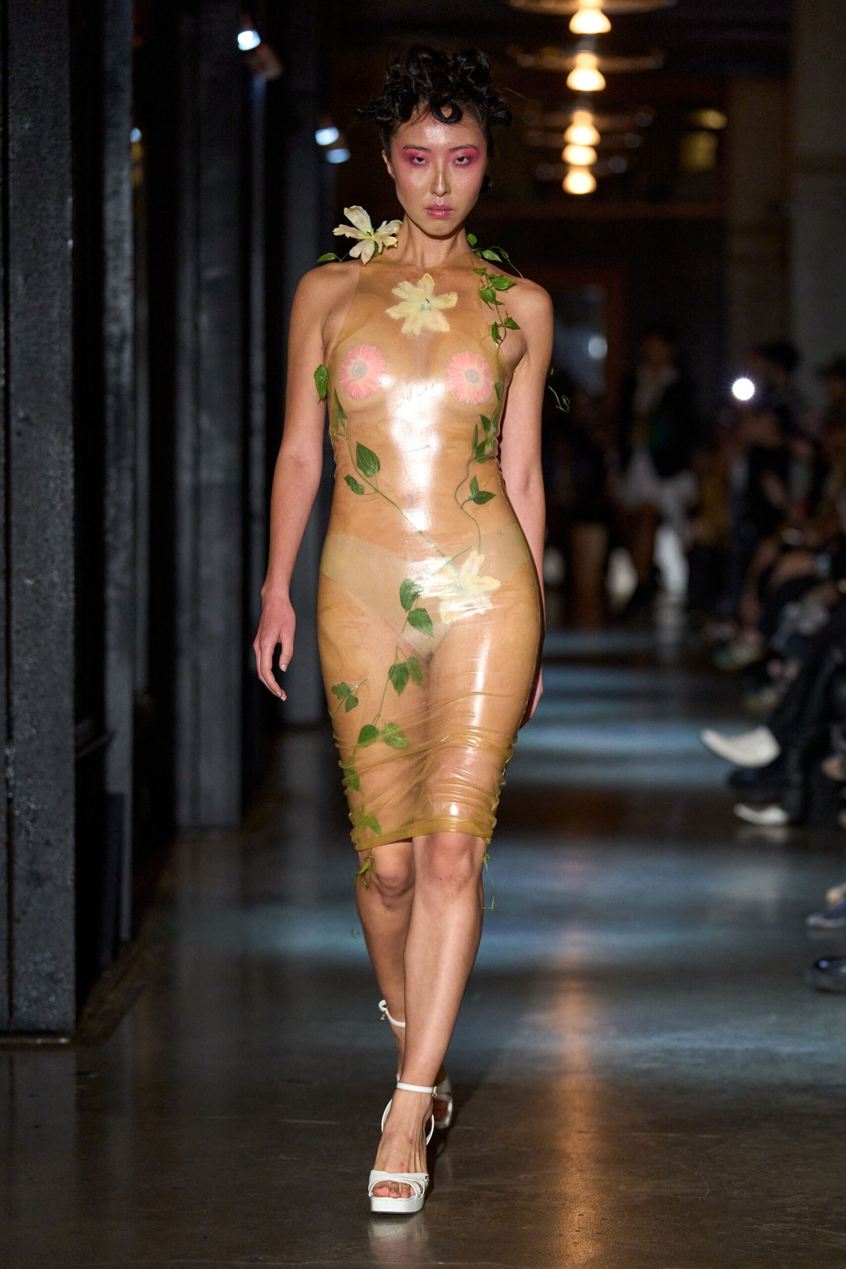 Transparent tan sheath, wrapped tight with real ivy and pale lilies trapped inside. White platform sandals with thin ankle straps. For carrying flowers home through heat that turns everything slightly sticky.