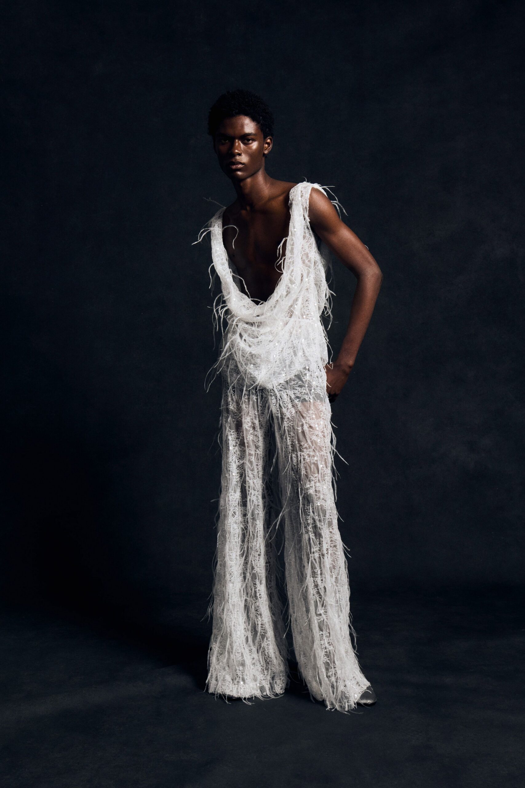 Ivory net top draped into a plunging cowl, threaded with wispy feather strands. Sheer lace wide-leg trousers, fringed all over with loose eyelash fibers. Silver pointed shoes just visible under the pooling hems. For opening the motel door at dawn still wearing last night's glitter.