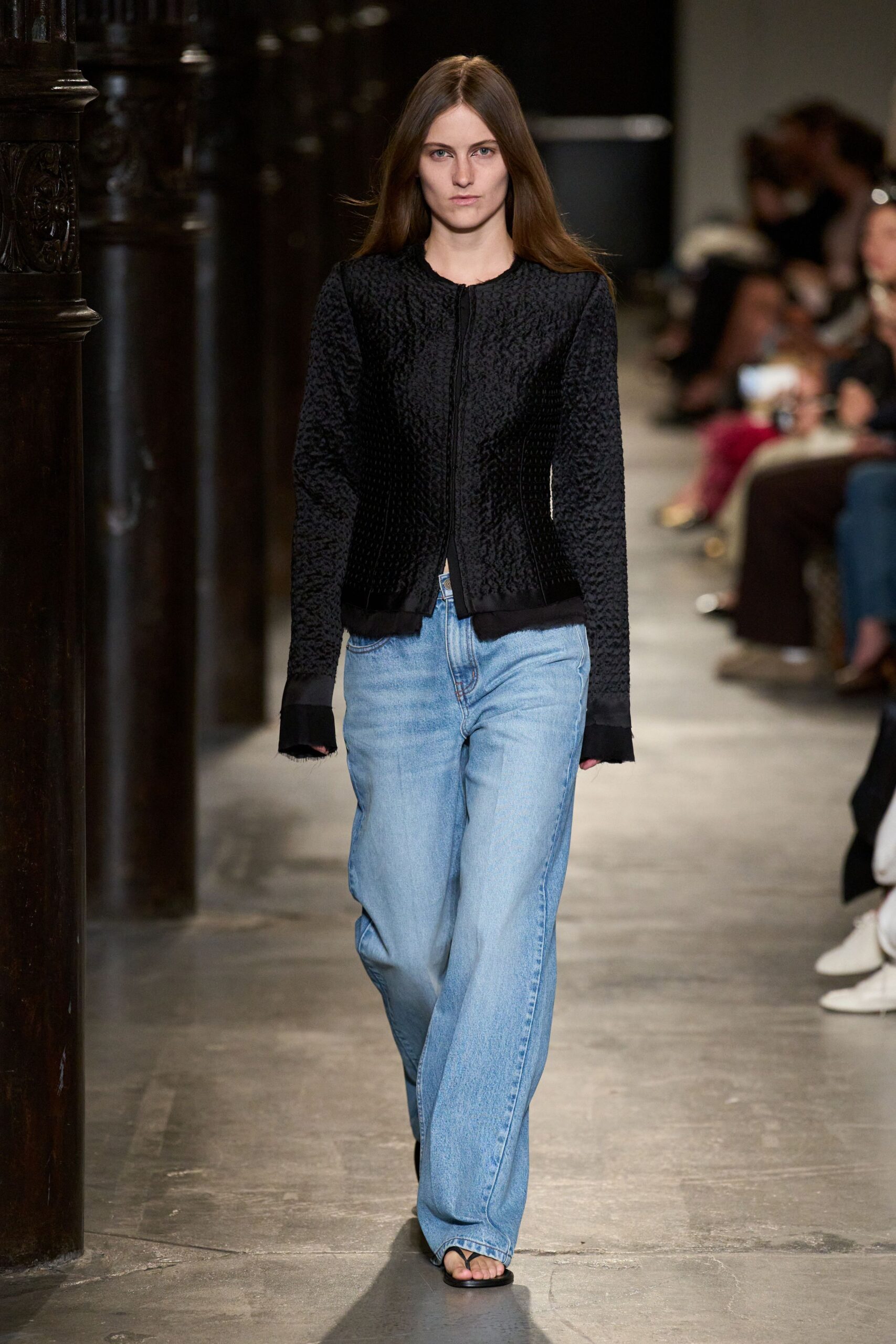 Black puckered cardigan, raw-edged cuffs and hem flaring over the hands. Pale stonewashed jeans, cut wide and pooling over the instep. Flat black thong sandals. Sunday museum hour, coat checked and nowhere you need to hurry.