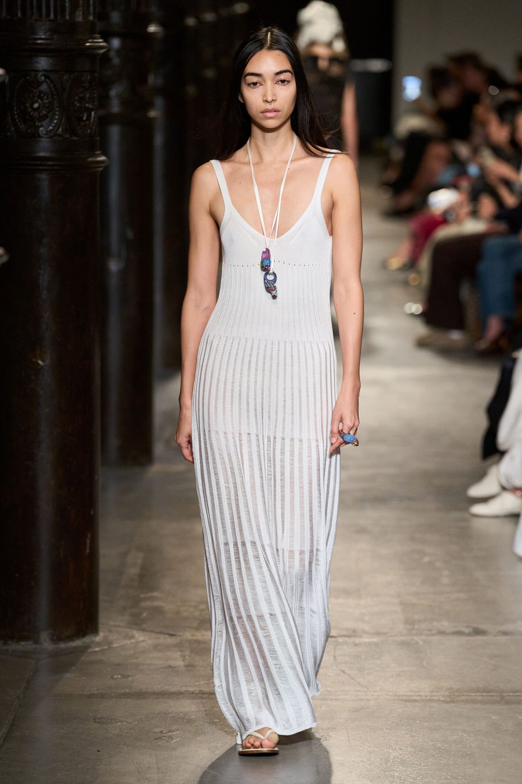 Pale grey ribbed knit column dress, sheer between the vertical channels. Long white cord necklace with stacked purple and blue carved pendants. Chunky beaded ring in the same bright colors. Flat white thong sandals. Walking back from a beach wedding with salt drying on your shoulders.