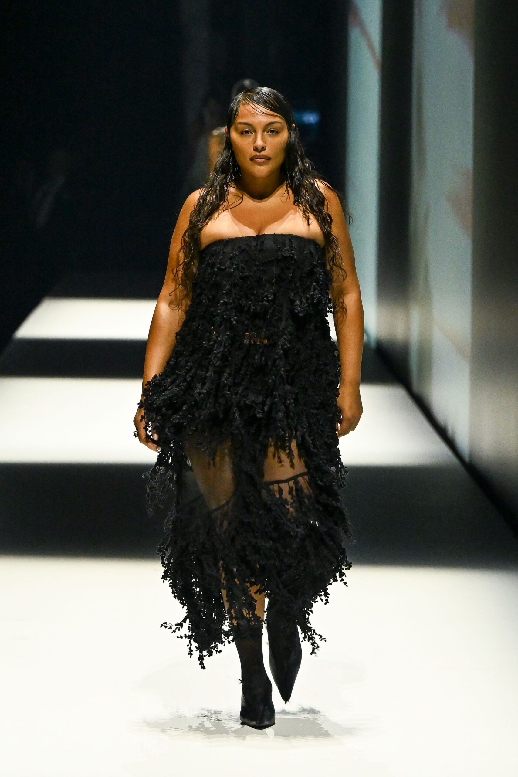 Black strapless dress shagged with knotted fringe over a sheer trailing hem. Black pointed boots disappearing under the gauze. Crossing a hotel lobby after midnight with rain still in your hair.