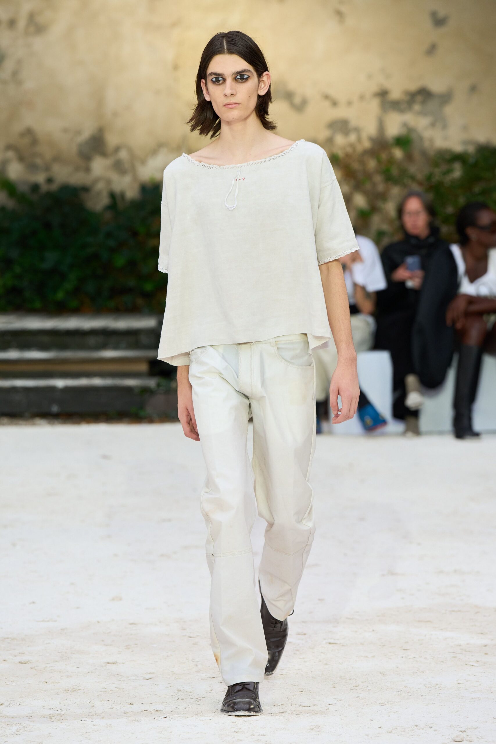Washed ivory top with lace edging and a tiny loop tie. Cream straight-leg jeans, dusty at the pocket curve and hems. Dark square-toe boots with scraped leather at the tip. Crossing a sunstruck cloister courtyard after rinsing paint from your hands.