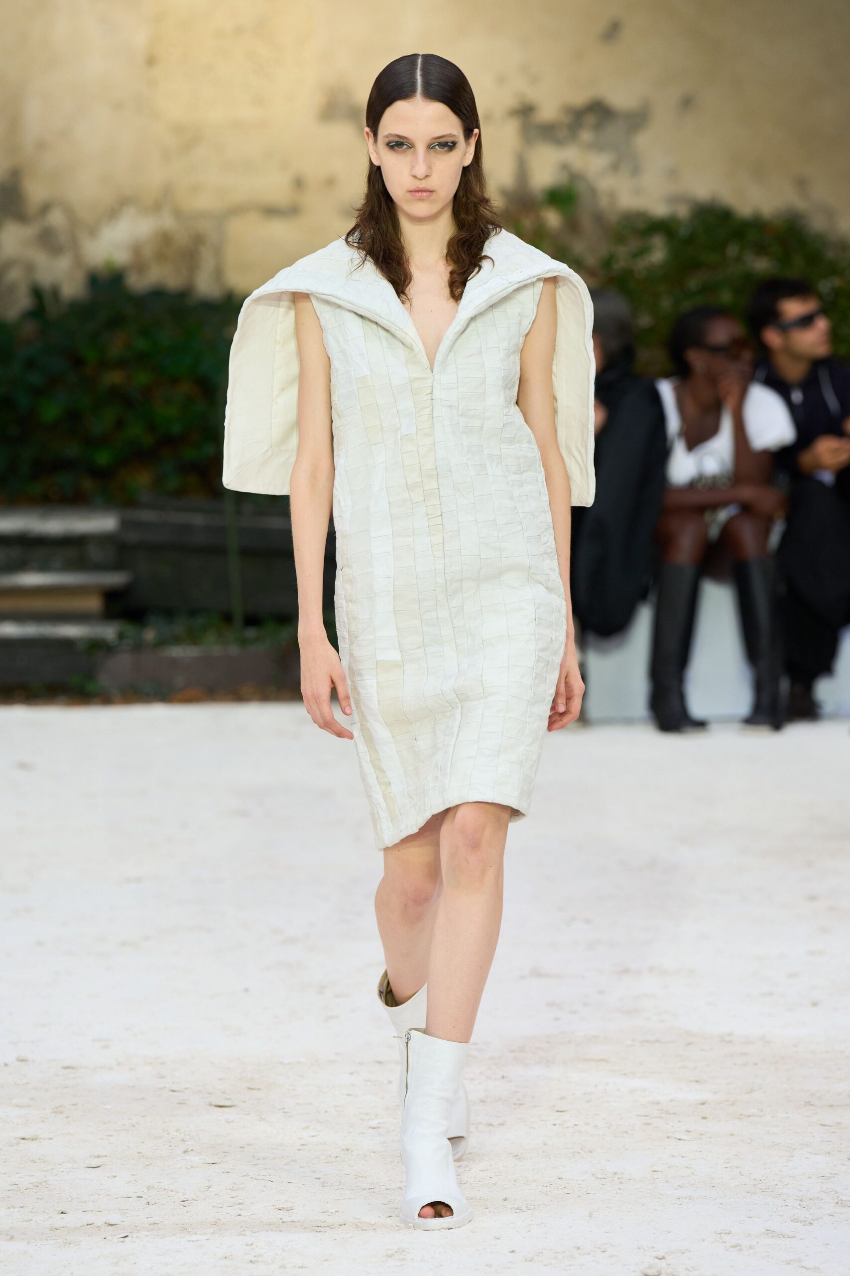 Pale quilted dress in narrow grid panels, with a padded cape collar. White peep-toe ankle boots with a front zip. Crossing a monastery courtyard just after the stone lets go of noon heat.