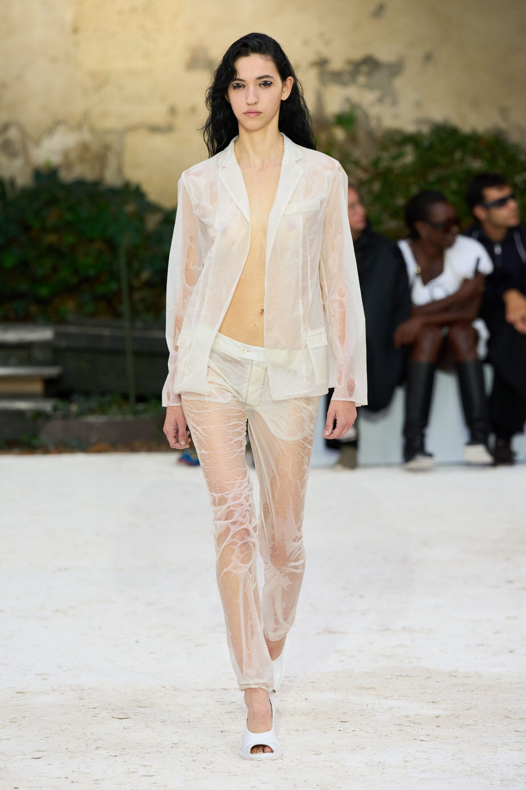 Sheer milky blazer with welt pockets and a bare plunging front. Matching translucent trousers, marbled with pale cream swirls over the legs. White peep-toe mules. Walking across a sunblasted courtyard just after someone hosed the stone down.