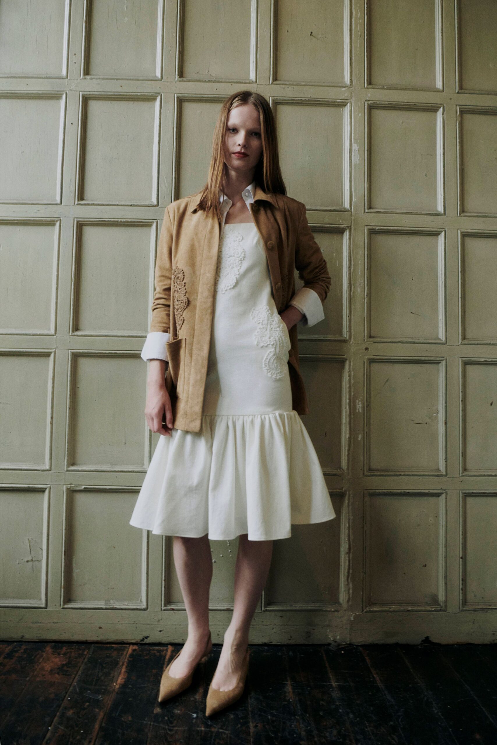 Biscuit suede jacket with white shirt cuffs turned sharply back. Ivory shift dress, soutache appliques climbing the torso above a dropped flounce. Taupe suede pumps with narrow pointed toes. Afternoon in a drafty manor house, waiting for someone to unlock the library.